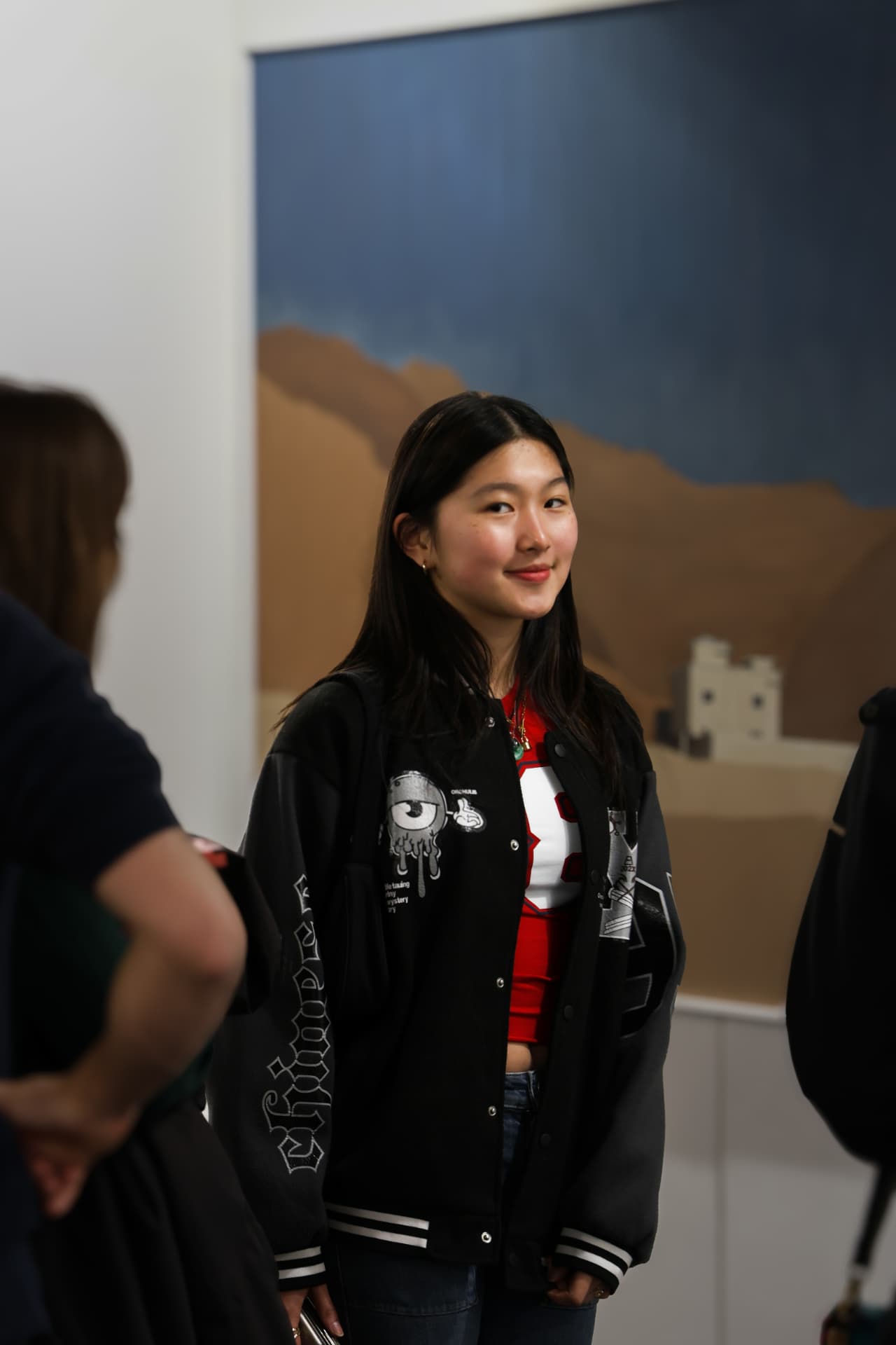 Visitor in a varsity jacket beside a desert landscape print