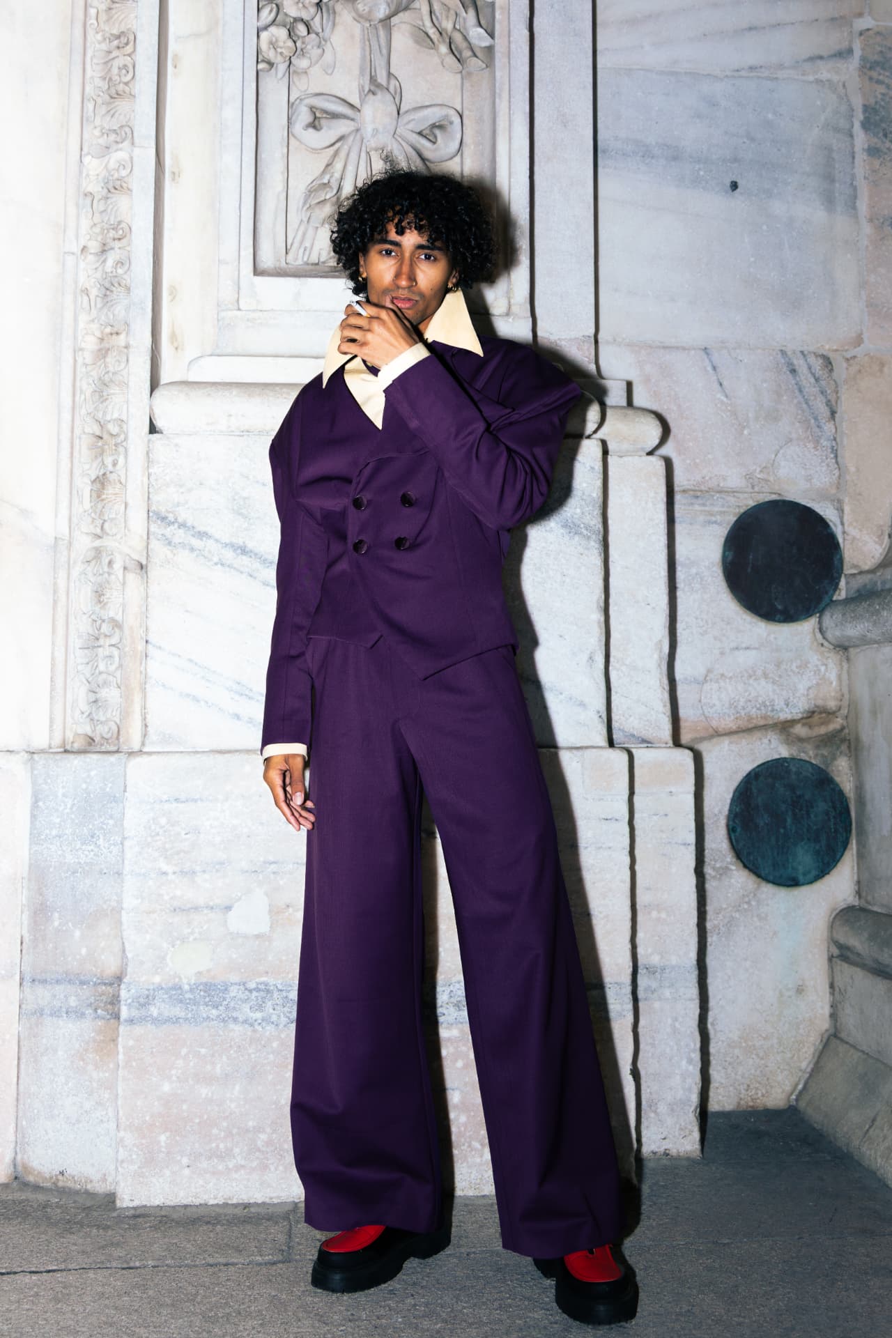 Model in a purple suit and red shoes against marble