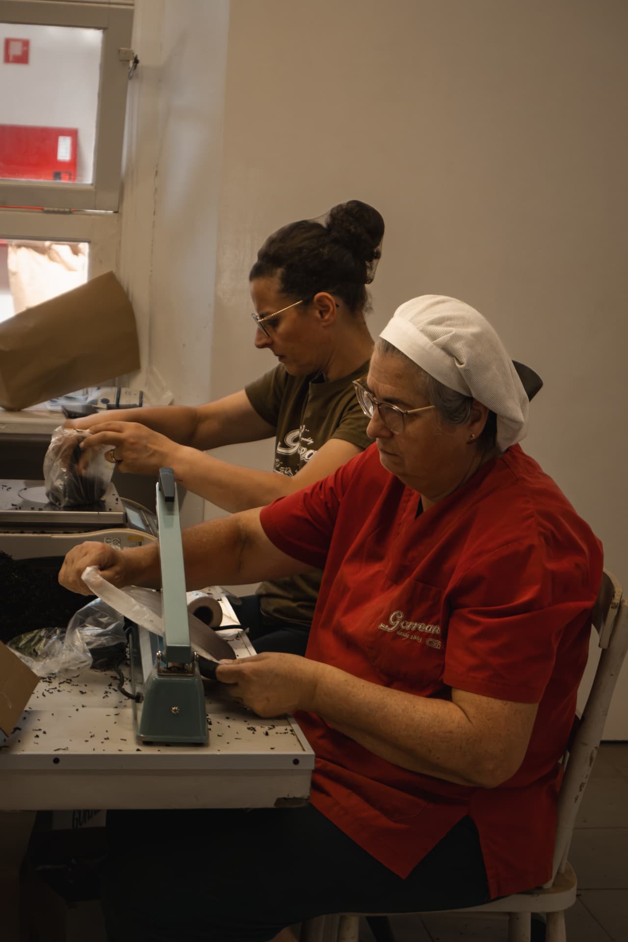 Two women sealing tea sachets at a factory table
