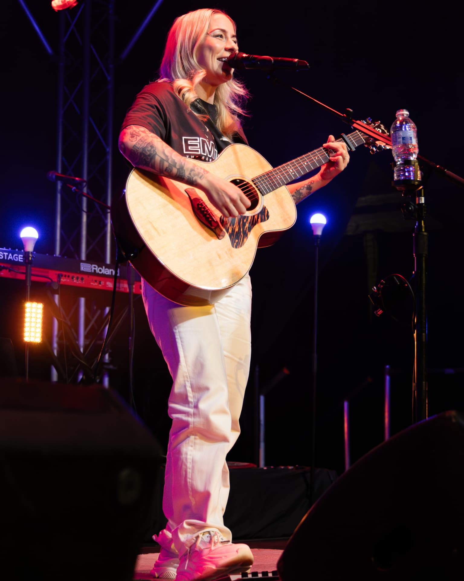 Lucy Spraggan singing full length with acoustic guitar in pink light