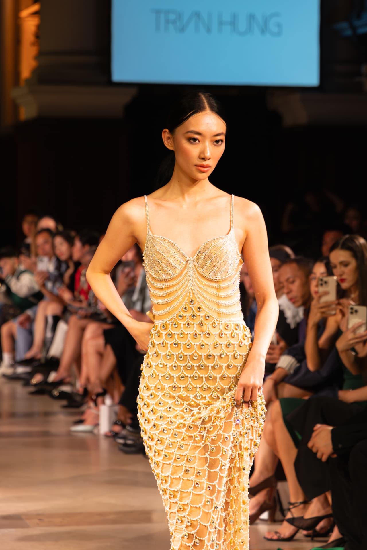 Model in a beaded gold gown on the Tran Hung runway