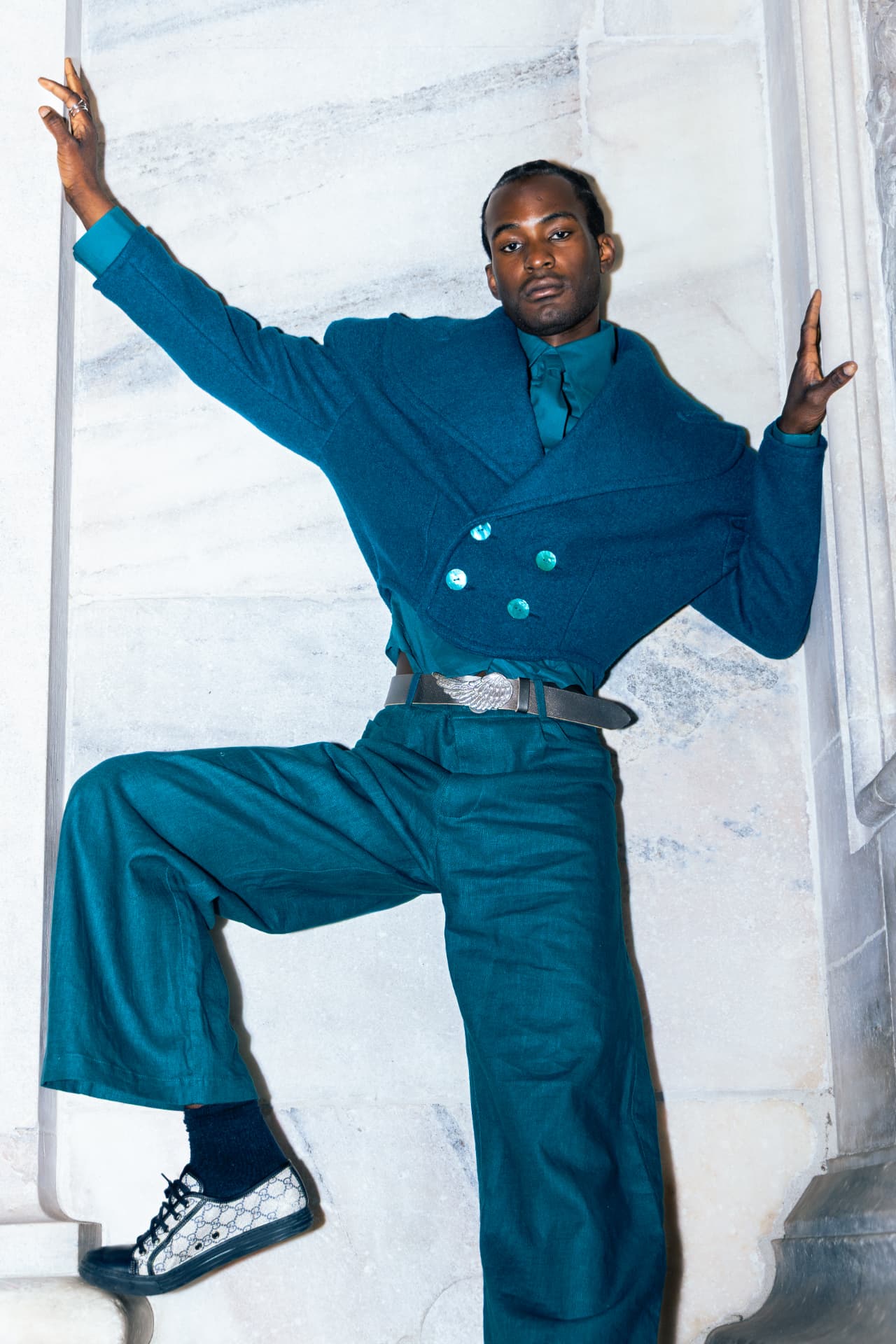 Model in a teal suit posed against marble