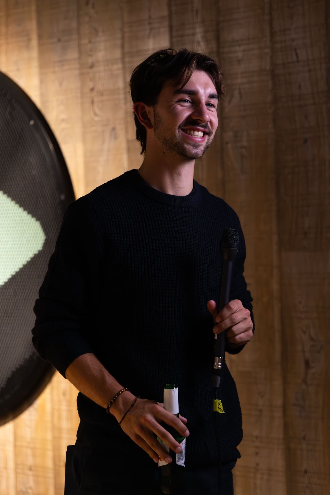 Speaker smiling with a microphone against a timber wall