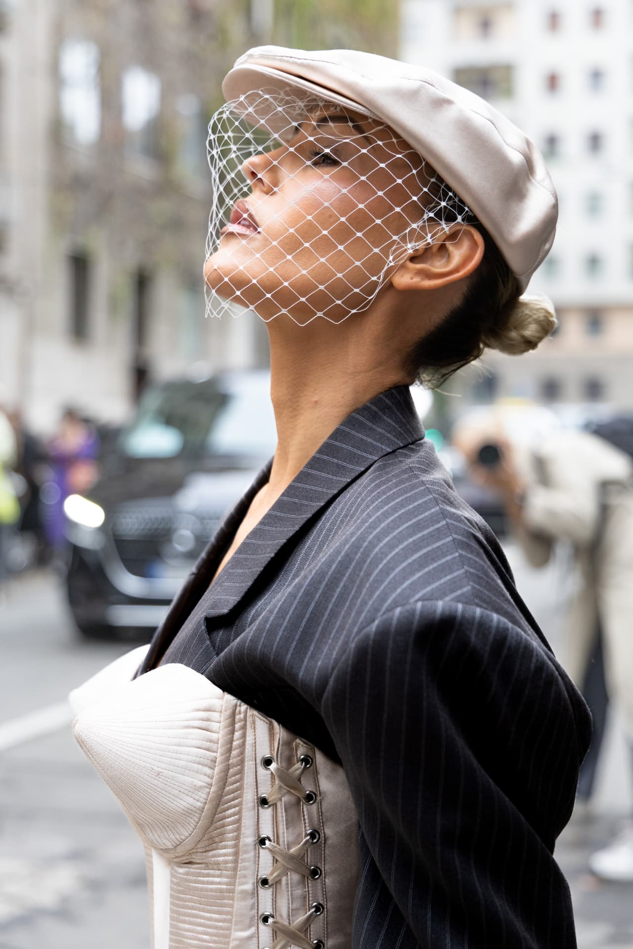 Guest in a pinstripe jacket and veiled cap on a city street