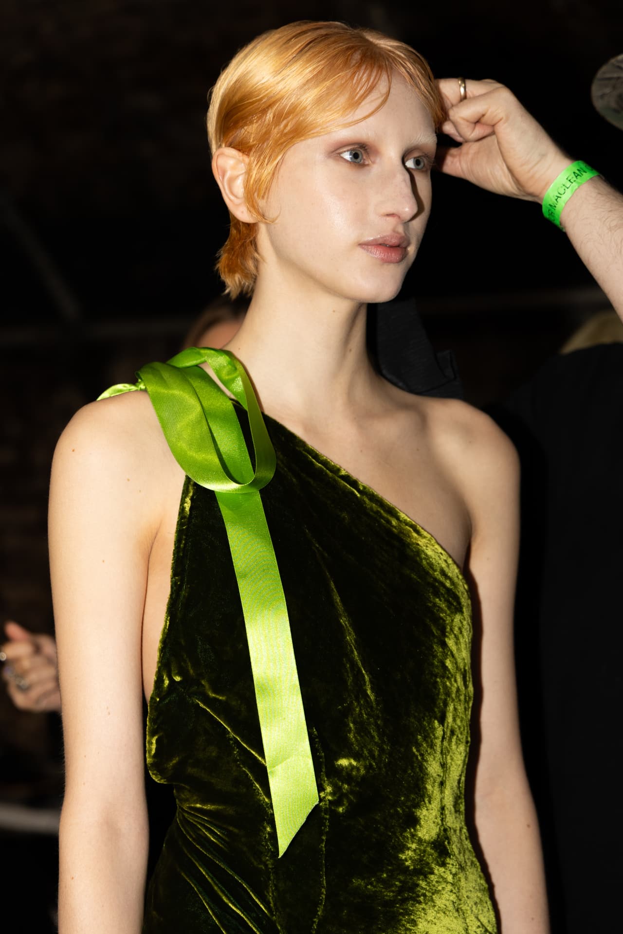Model in a green velvet one-shoulder dress being prepped backstage