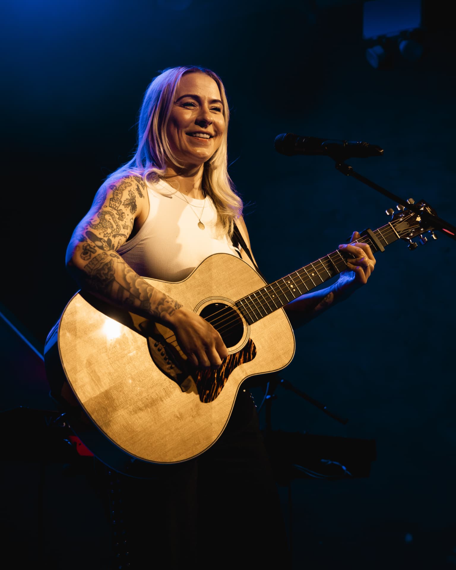 Lucy Spraggan smiling with acoustic guitar in blue light