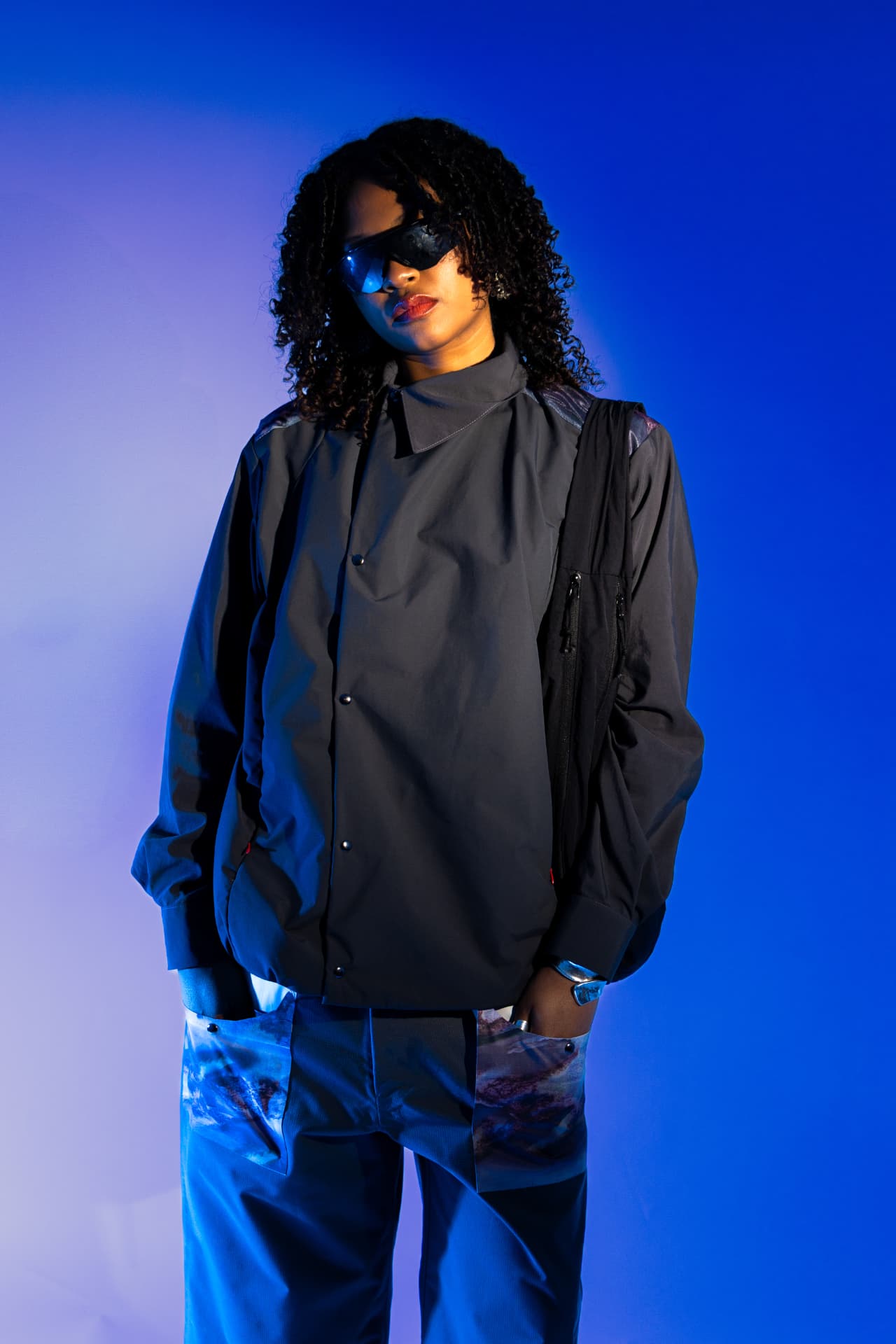 Model in a grey jacket and printed trousers on a blue gradient
