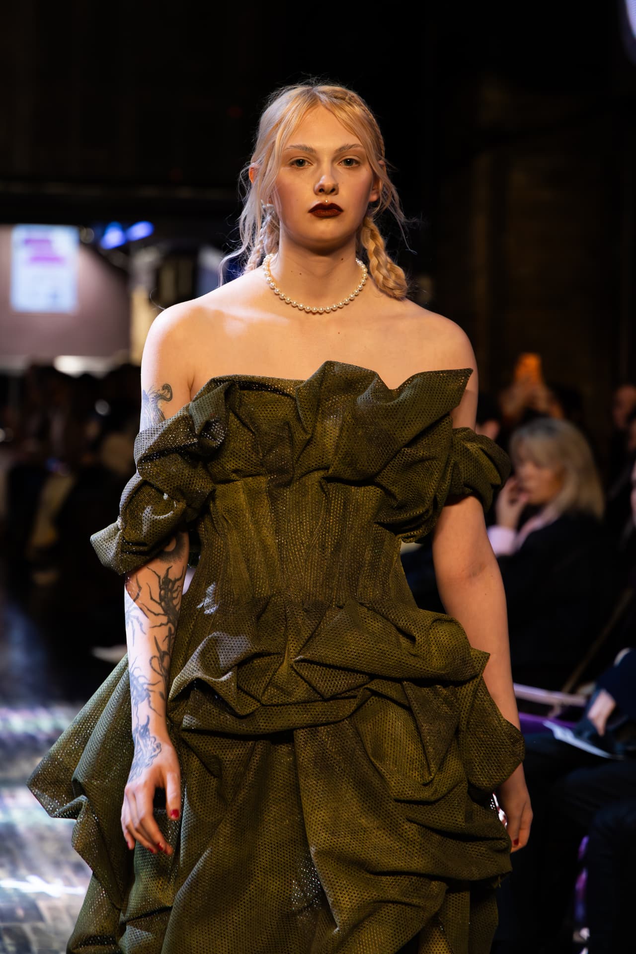 Model in a ruffled olive off-shoulder gown with a pearl necklace