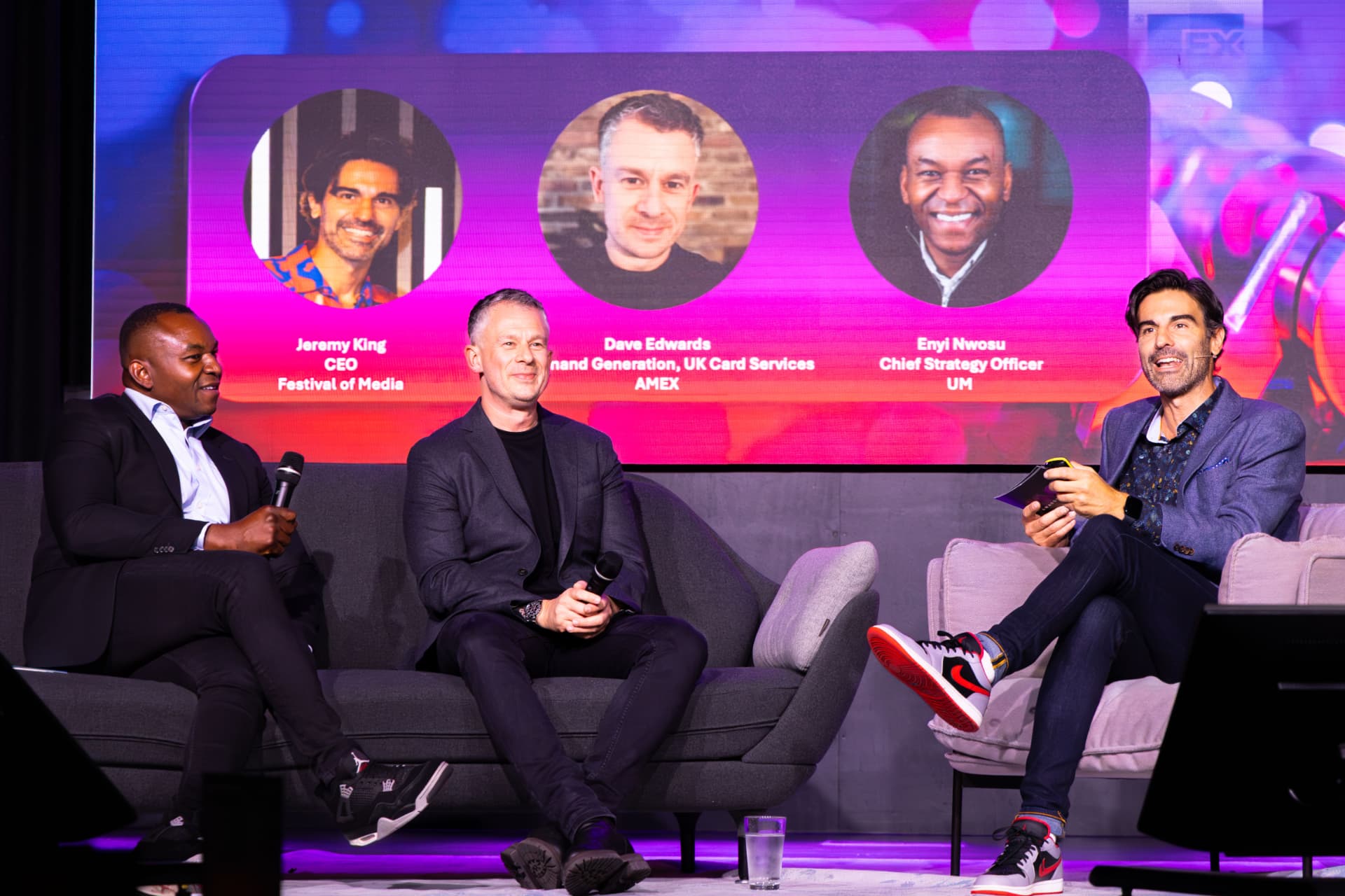 Three panellists laughing on stage in front of the speaker screen