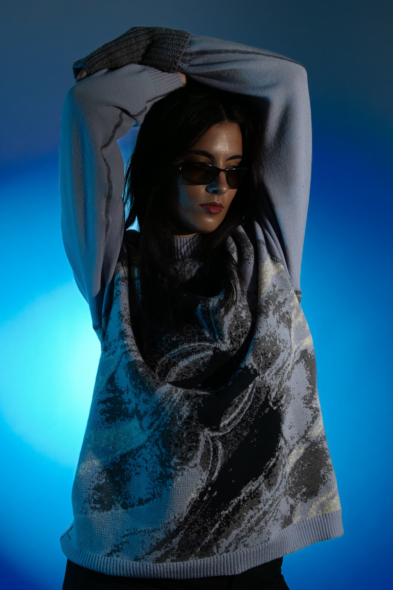 Model with arms raised in a printed grey knit on blue light