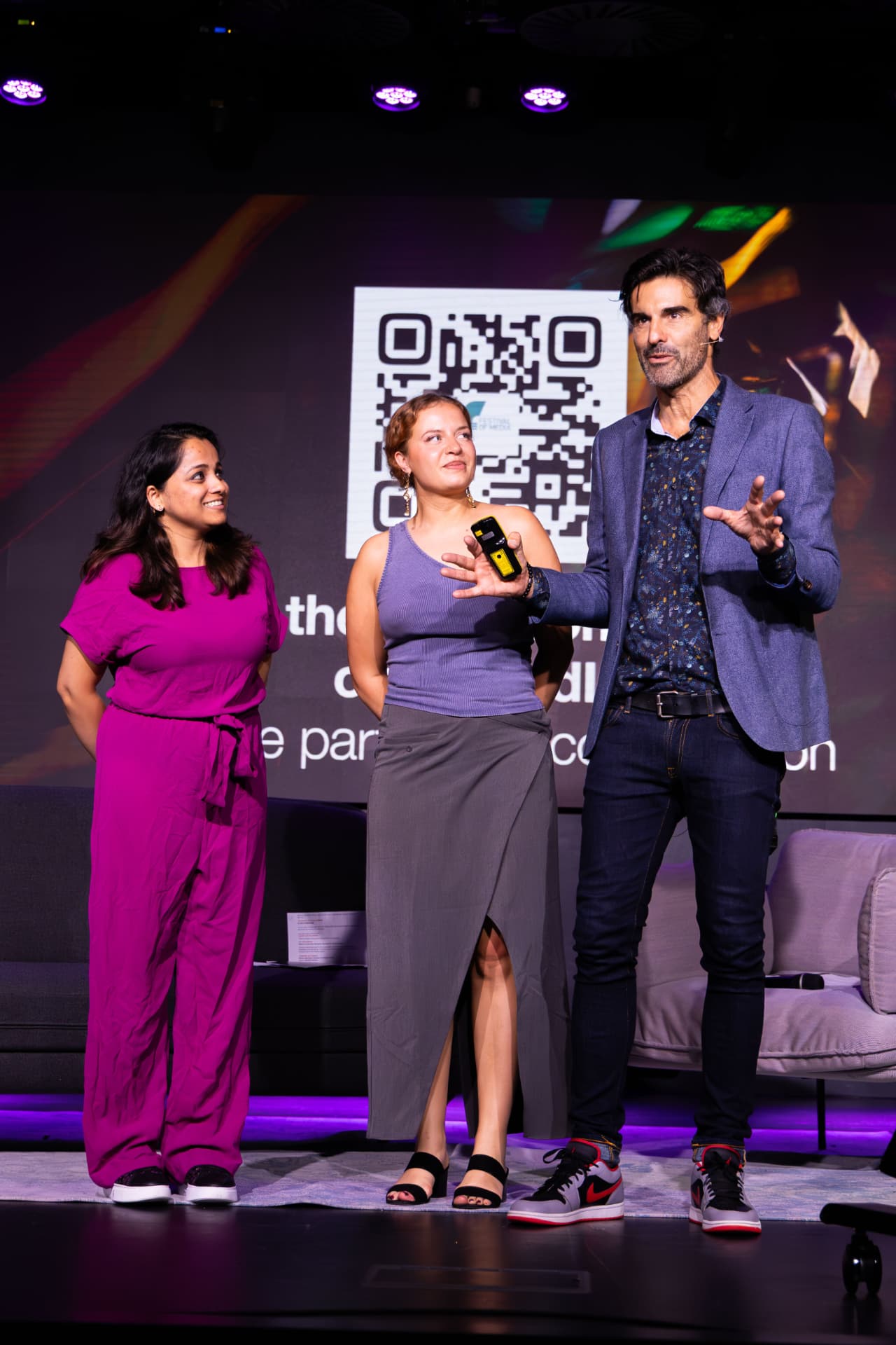 Host and speakers on stage beside a QR code slide
