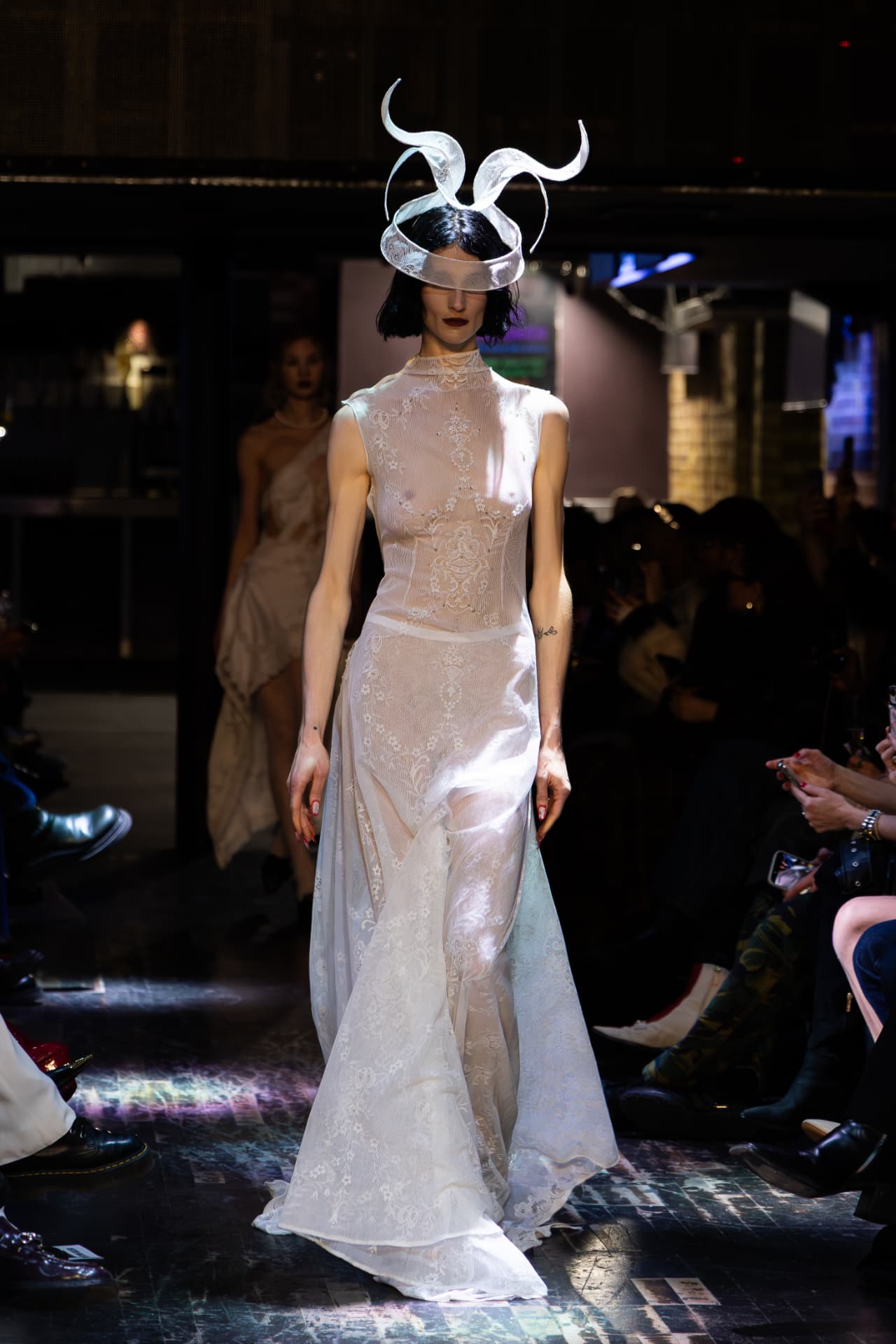 Model in a sheer lace gown with a sculptural headpiece