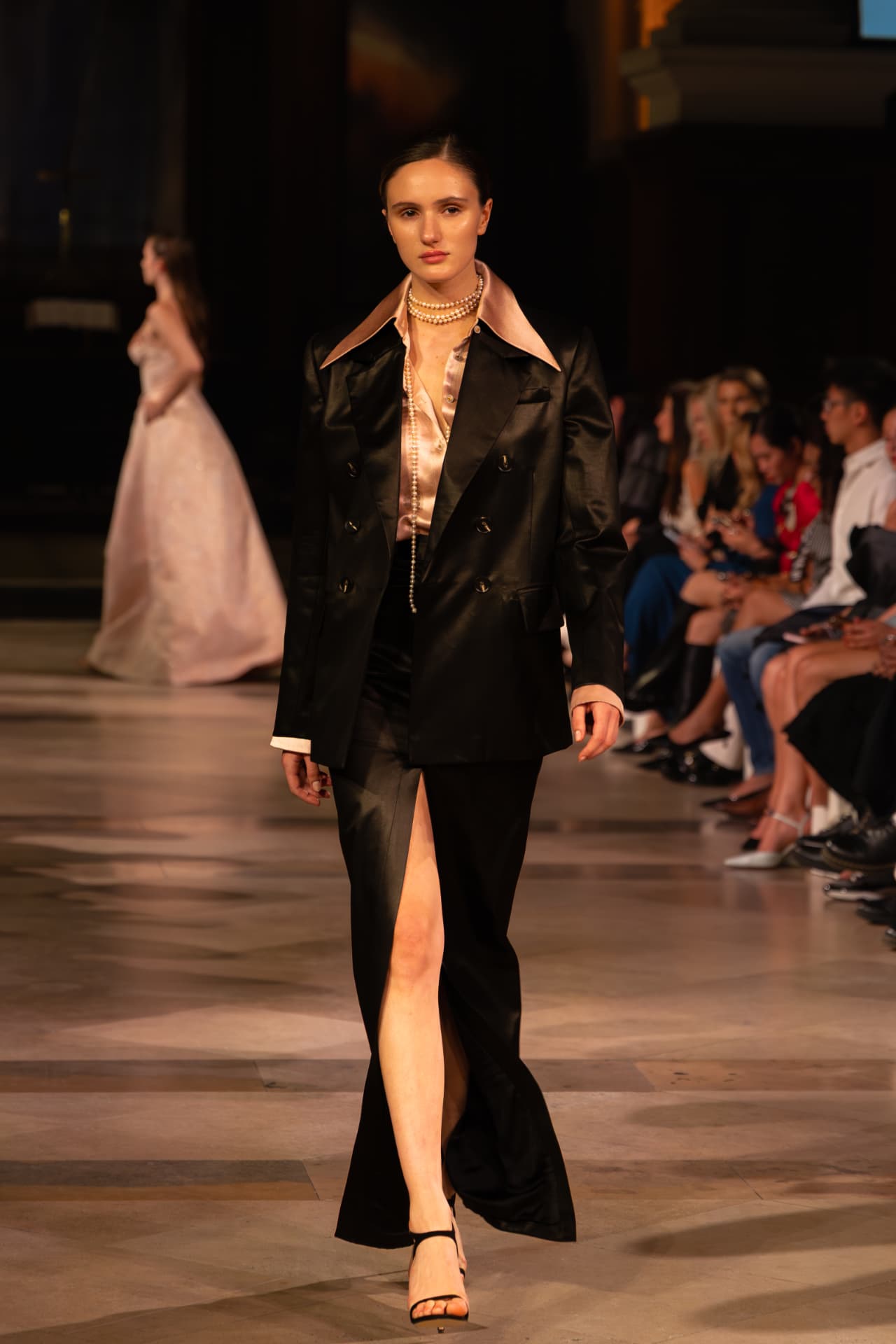 Model in a black satin suit with blush lapels and pearls