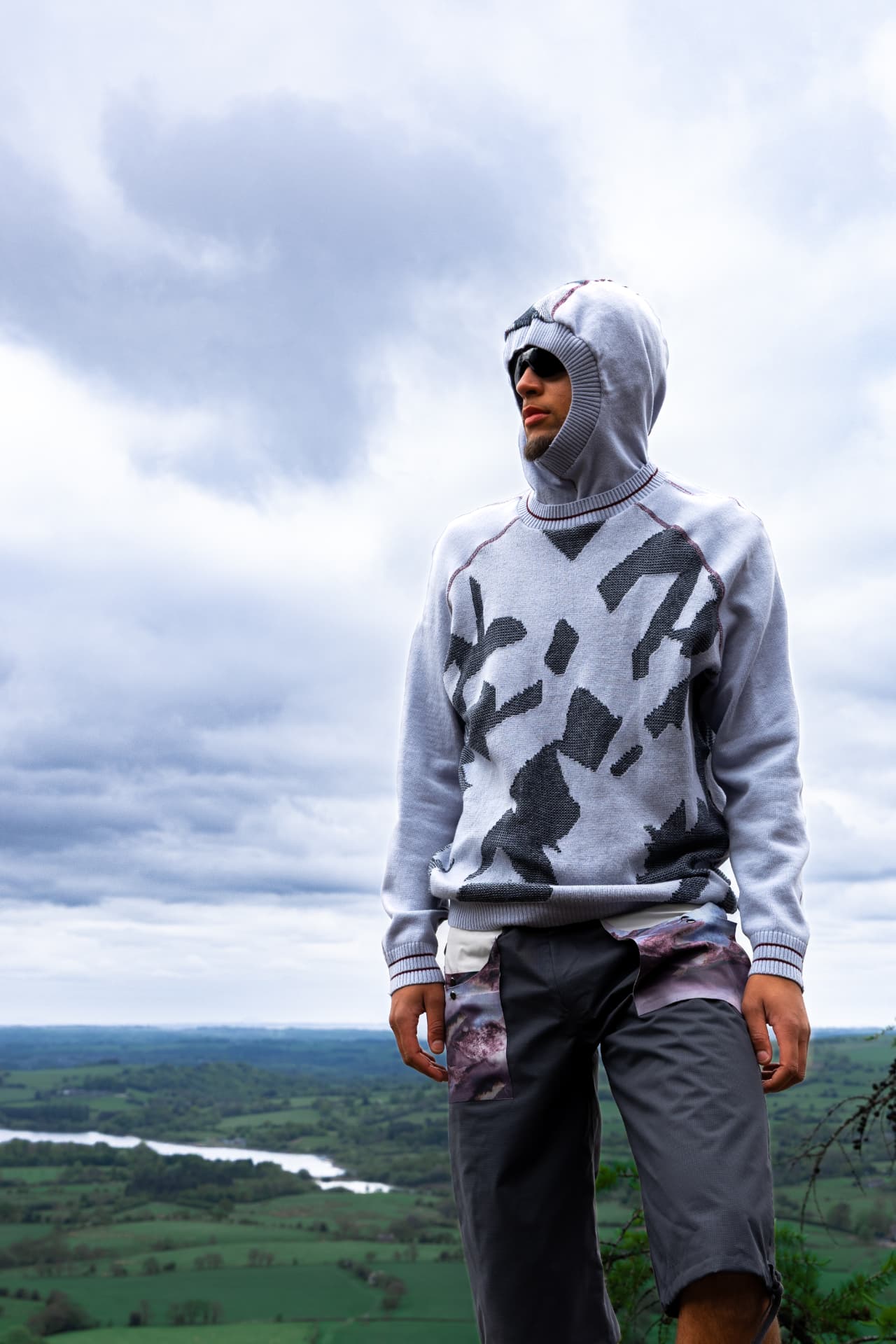 Model in a hooded grey knit standing above the countryside