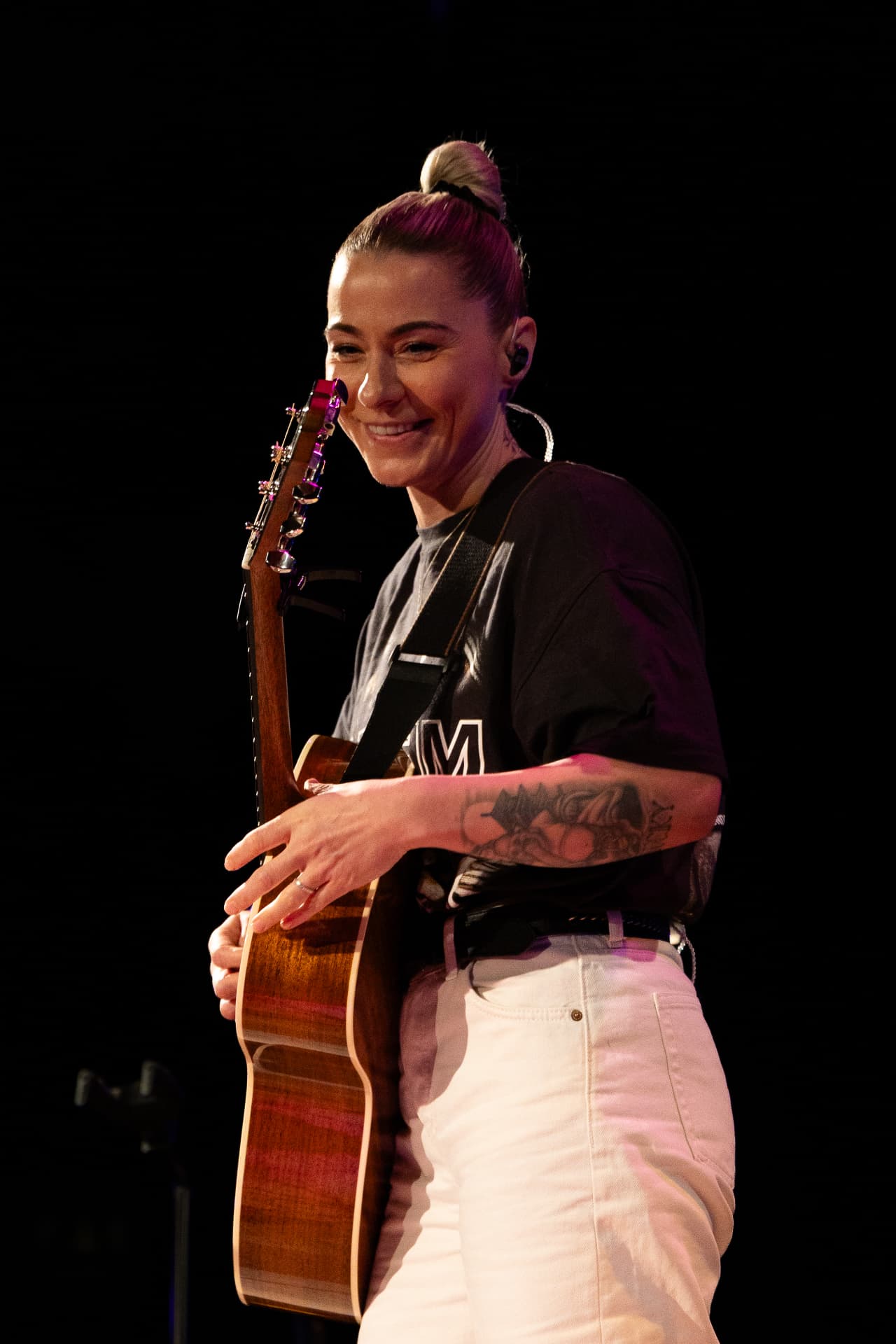 Smiling behind the guitar headstock in pink light