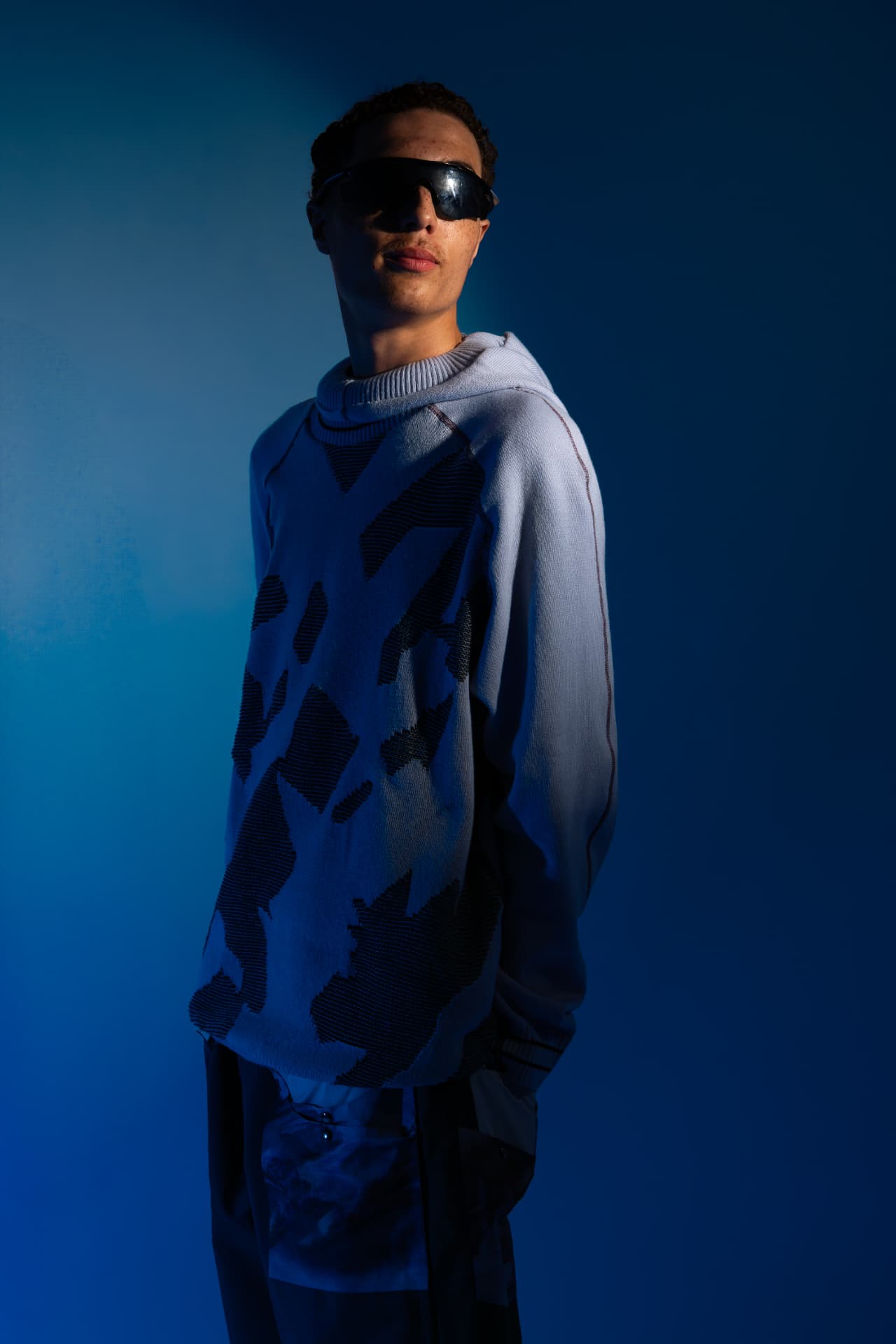 Model in a hooded printed knit against blue studio light