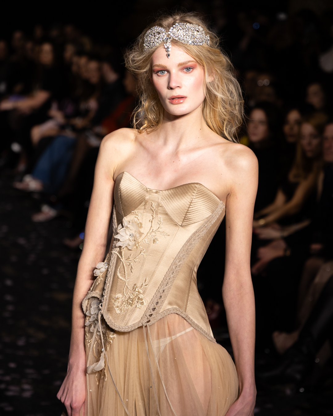 Model in an embellished corset gown and crystal headpiece on the runway