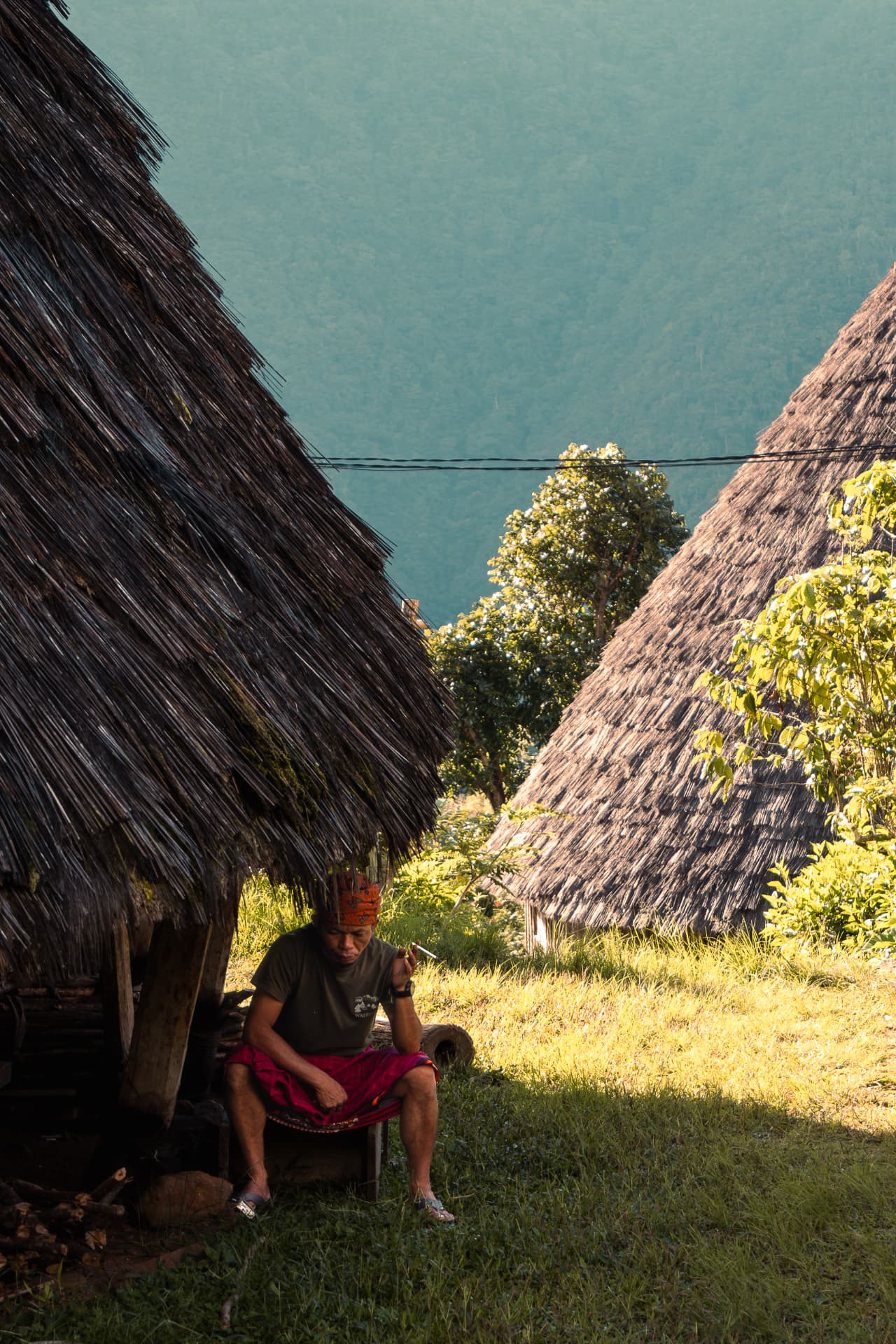 Man in traditional dress seated between two thatched-roof huts
