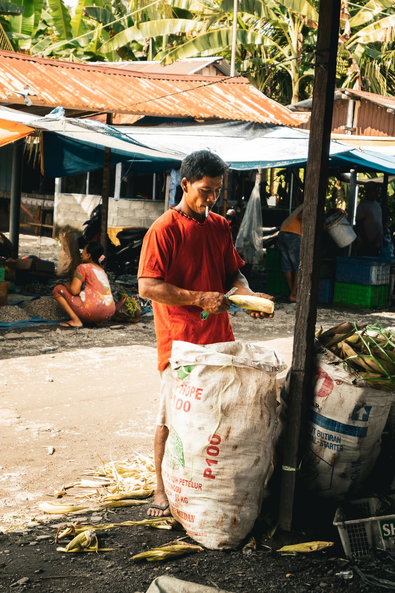 Man peeling corn beside hessian sacks at an outdoor market