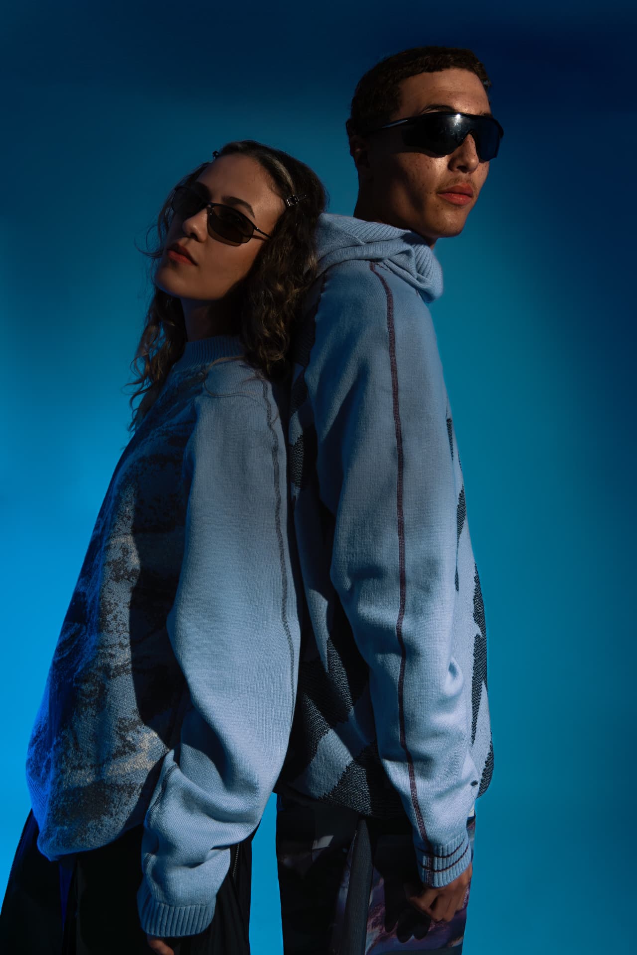 Two models back to back in pale blue knitwear on a blue backdrop