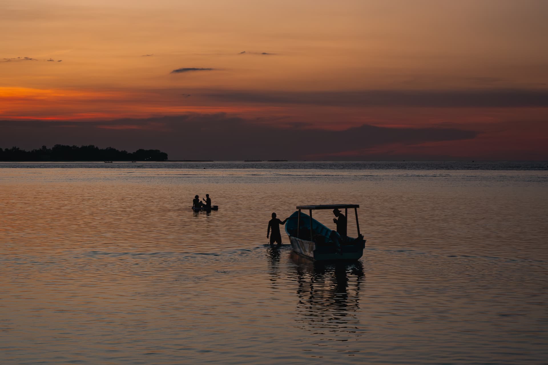 Silhouetted boat and figures in still water under a burnt-orange sunset