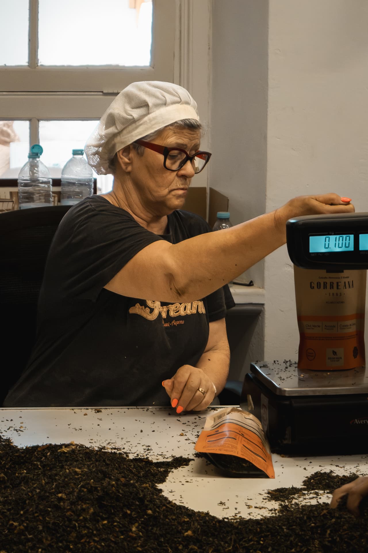 Woman weighing tea leaves at a factory workbench