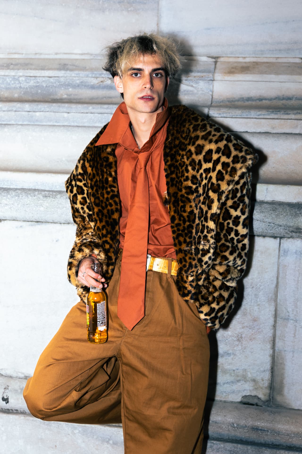 Model in a leopard coat and orange tie holding a bottle