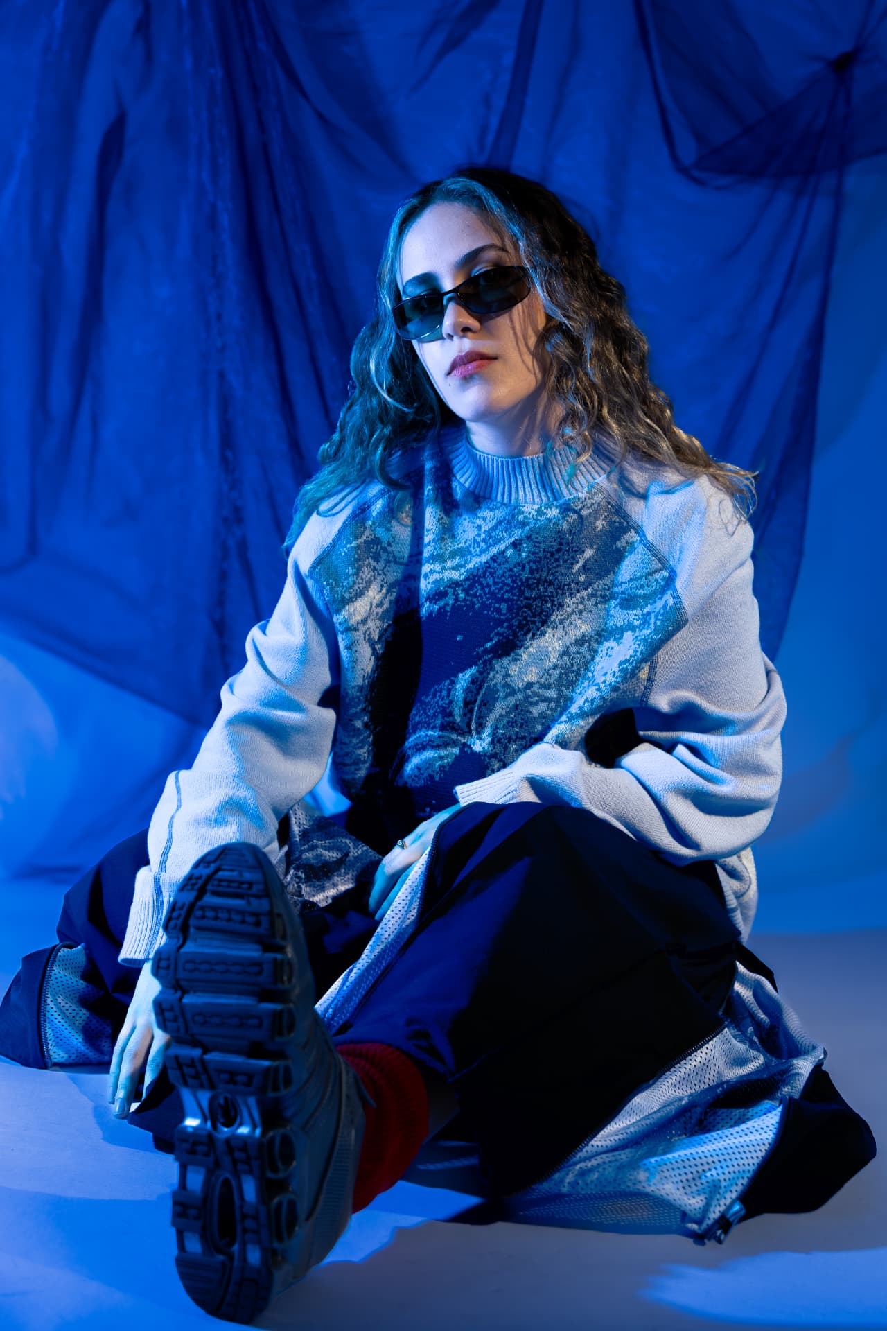 Model seated on the floor against blue draped fabric