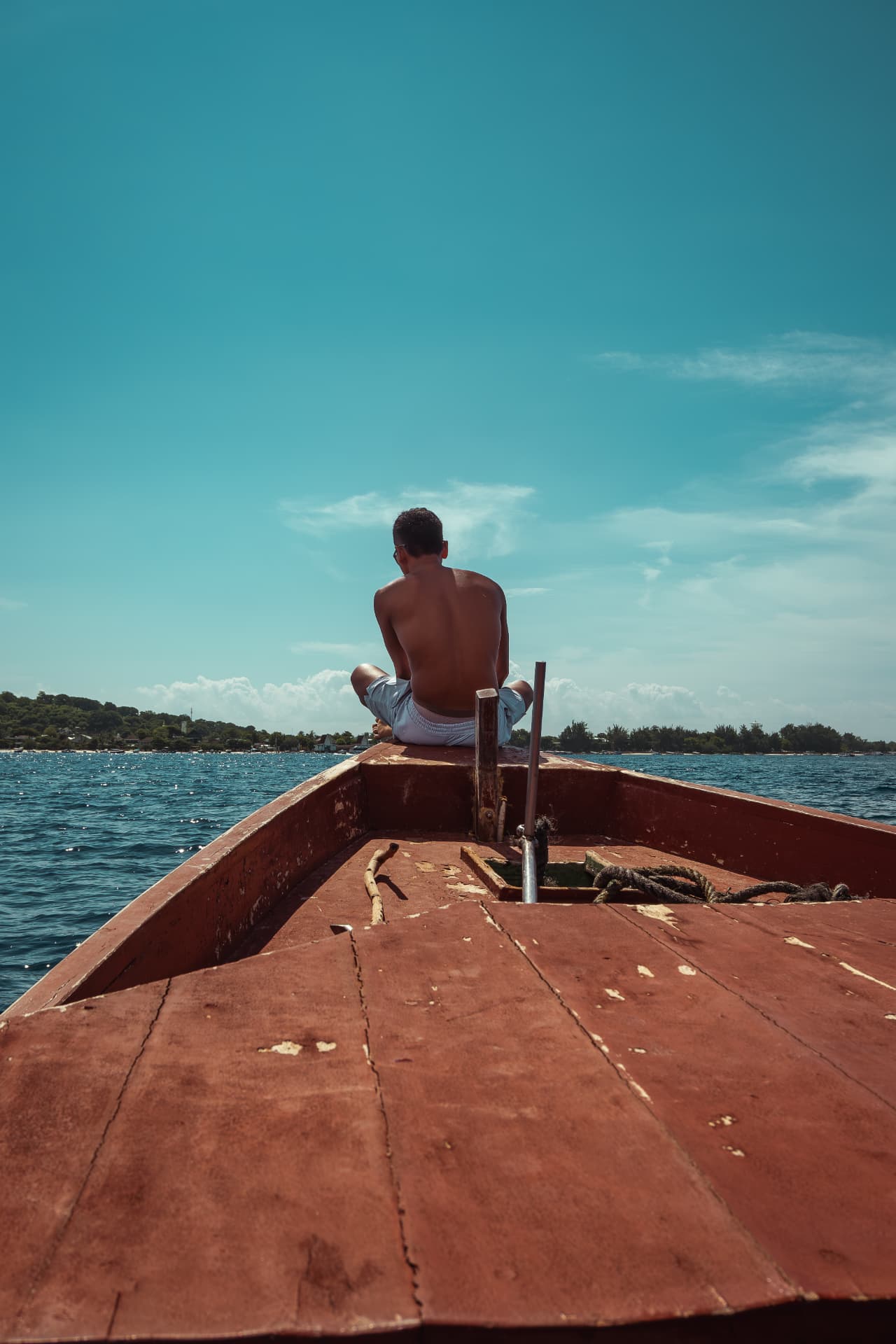 Man sitting cross-legged at the bow of a wooden boat on calm blue water