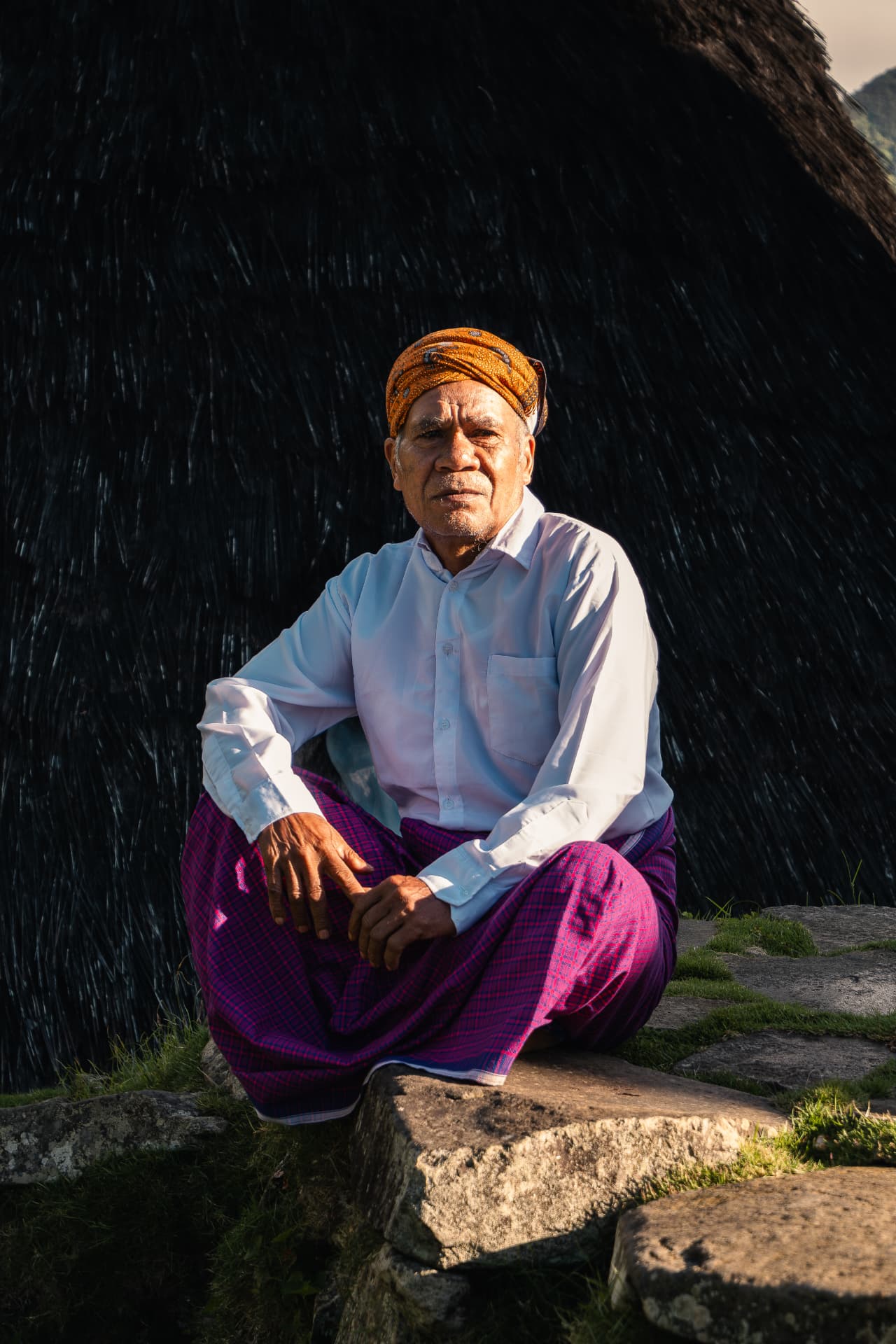 Elderly man in an orange turban and magenta sarong seated on stone steps