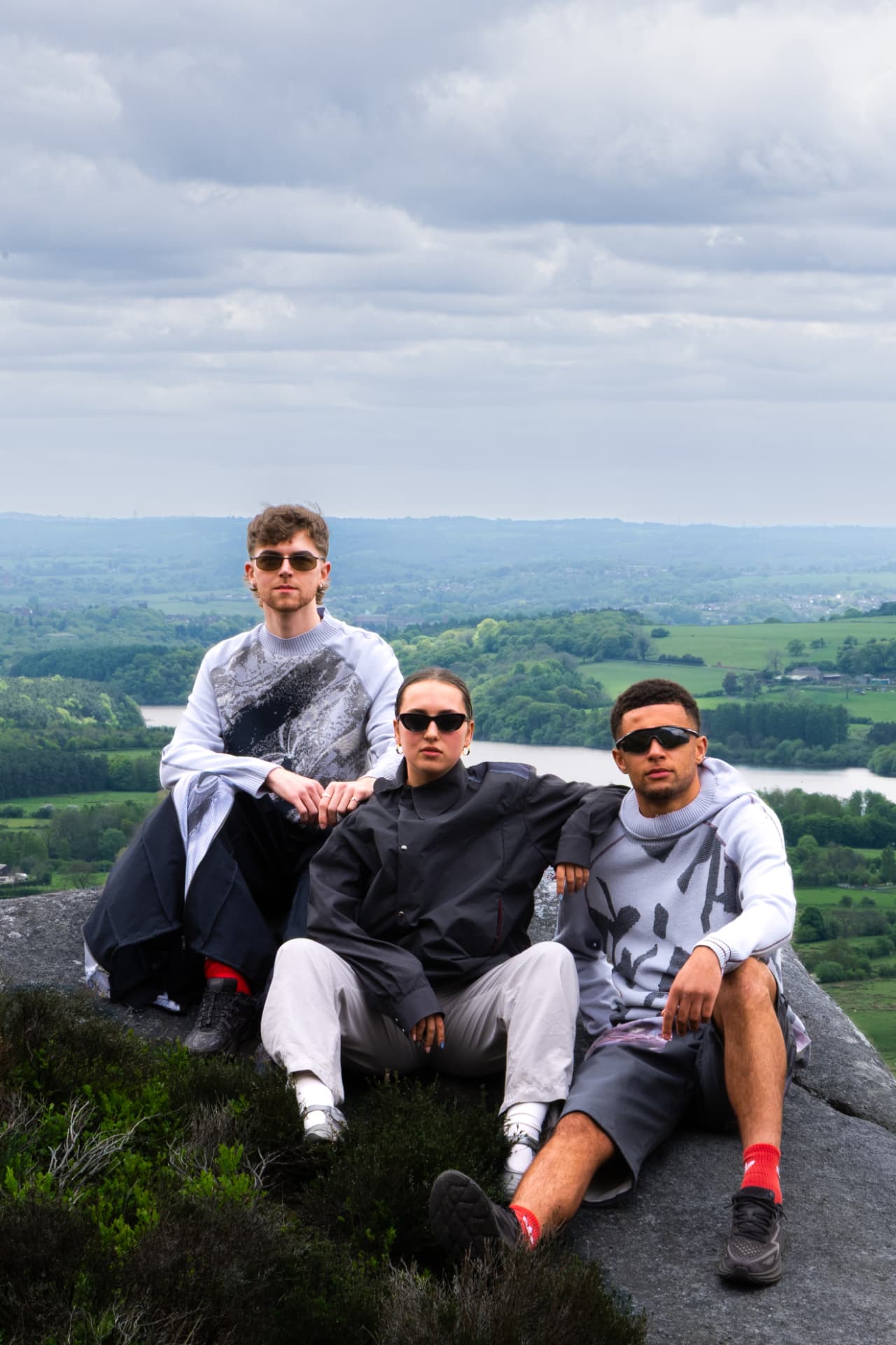 Three models seated on a rock above a green valley