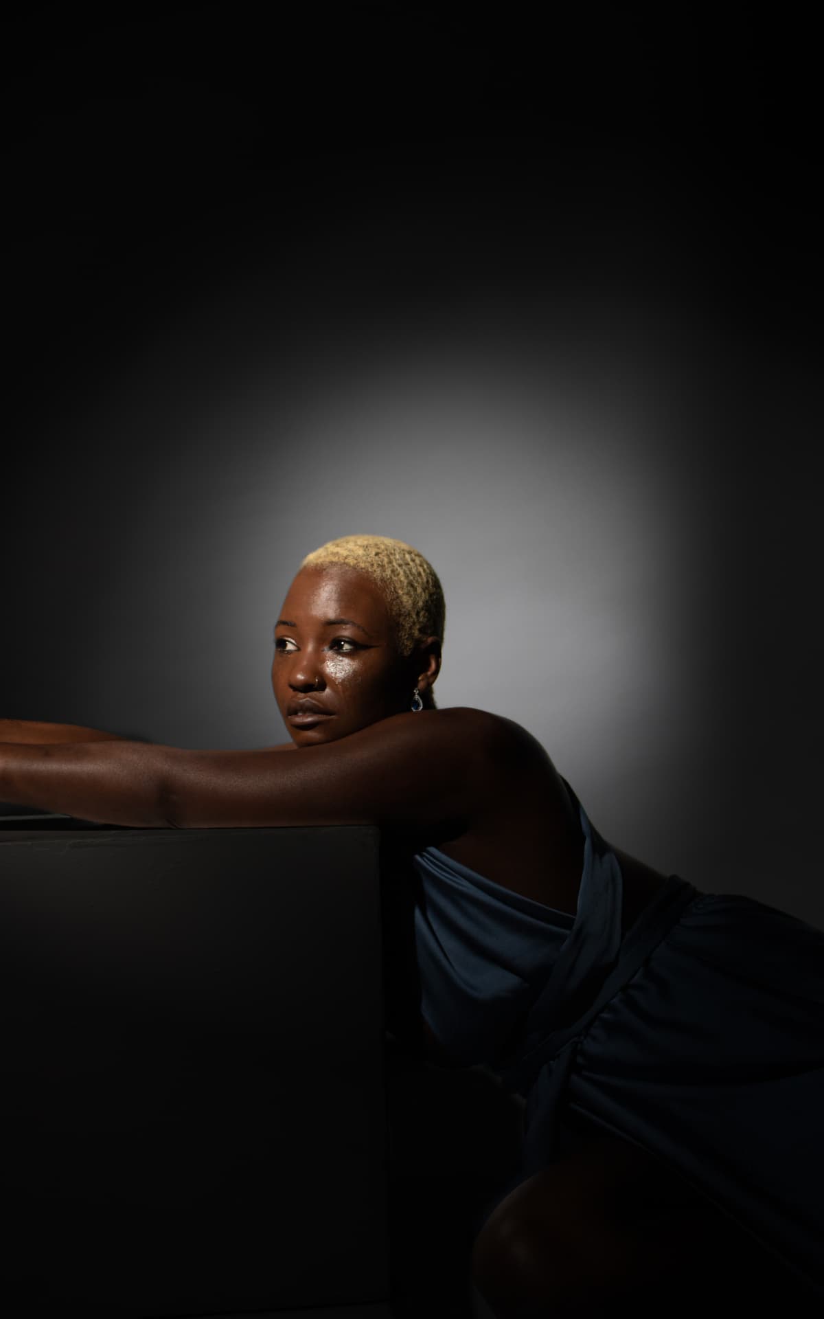 Model leaning on a plinth in a blue satin dress