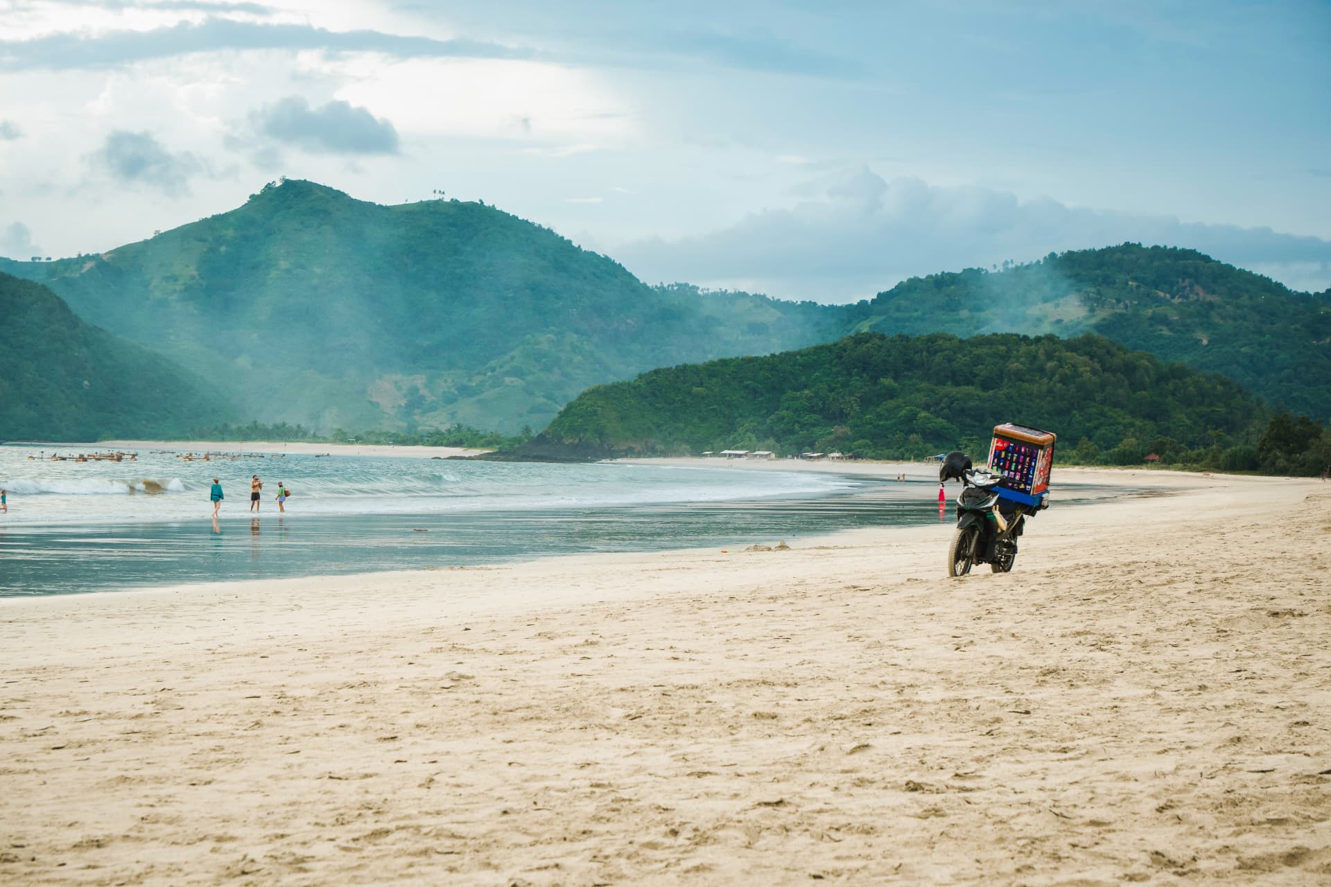 Motorbike vendor on a quiet beach with forested hills in the distance