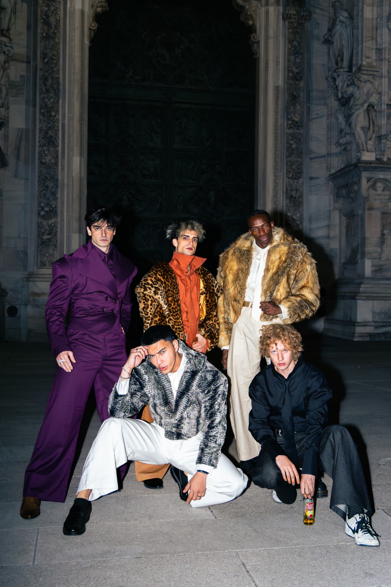 Group of models in bold tailored and fur coats outside a grand building