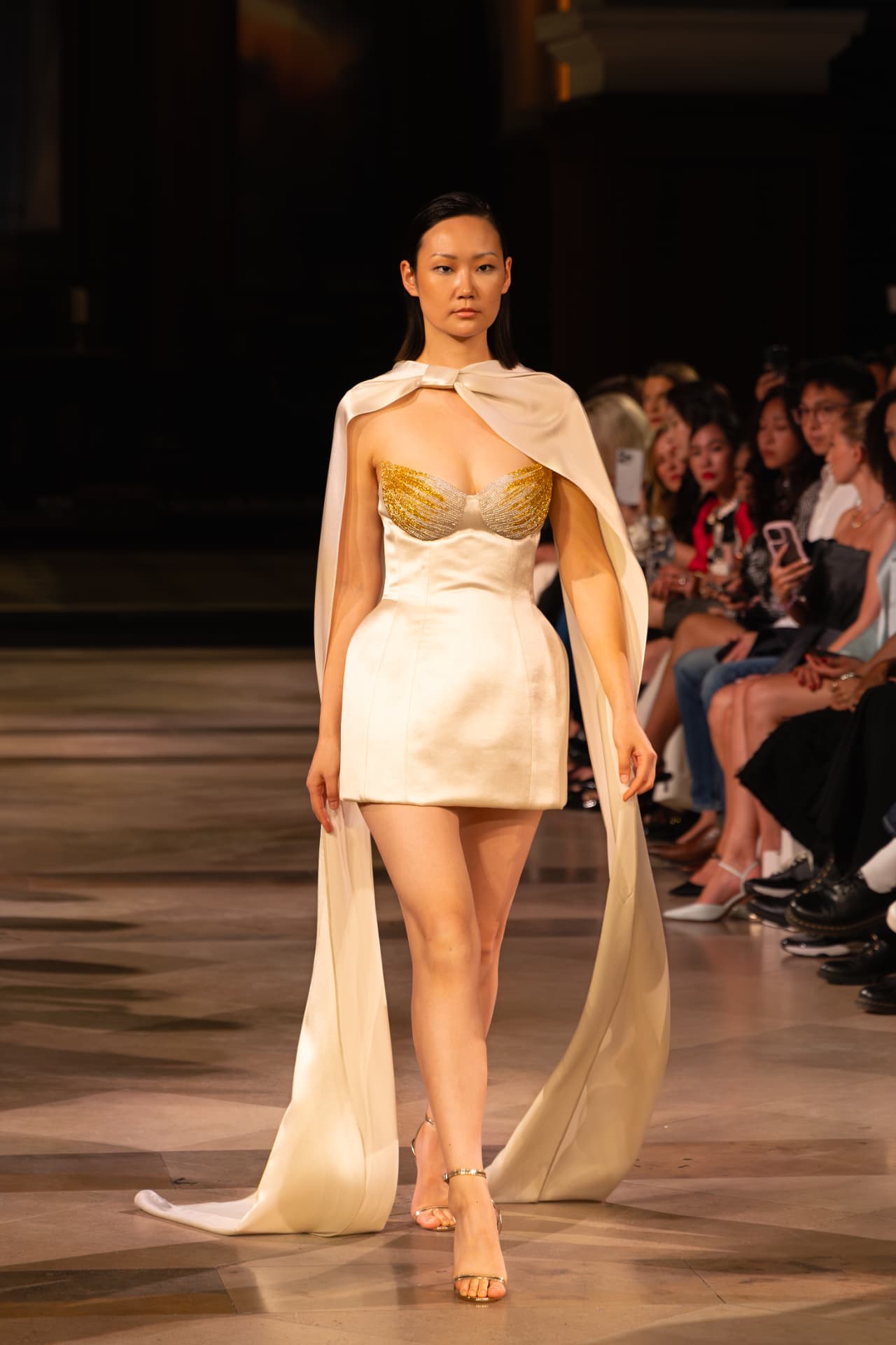 Model in a cream cape gown with a gold crystal bodice