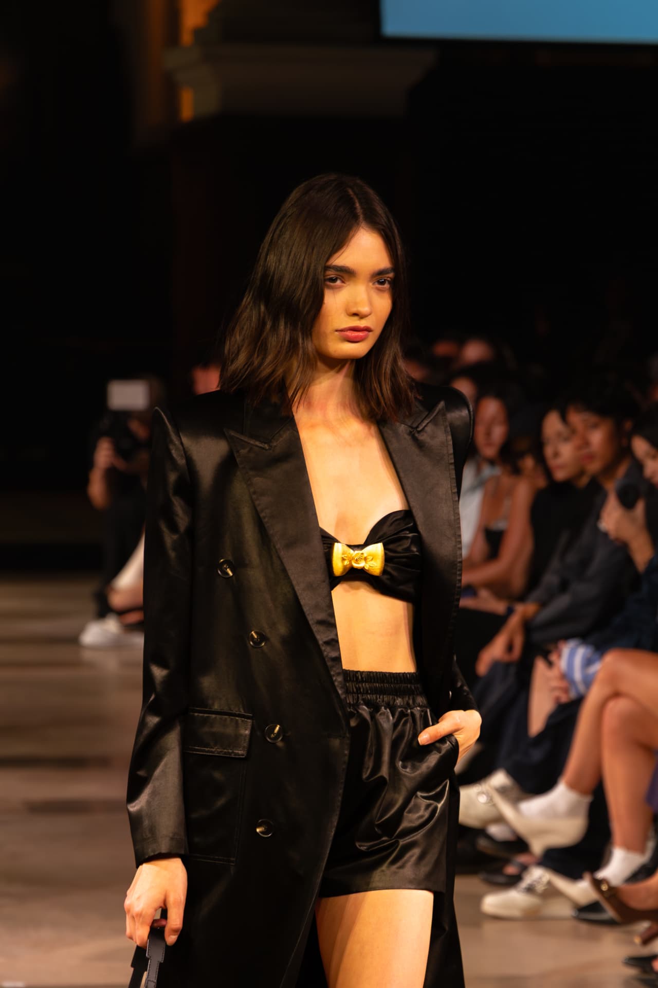 Model in a black satin blazer with a gold bow bandeau
