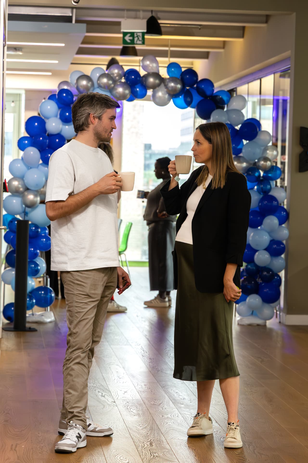 Two judges chatting over coffee by a balloon arch
