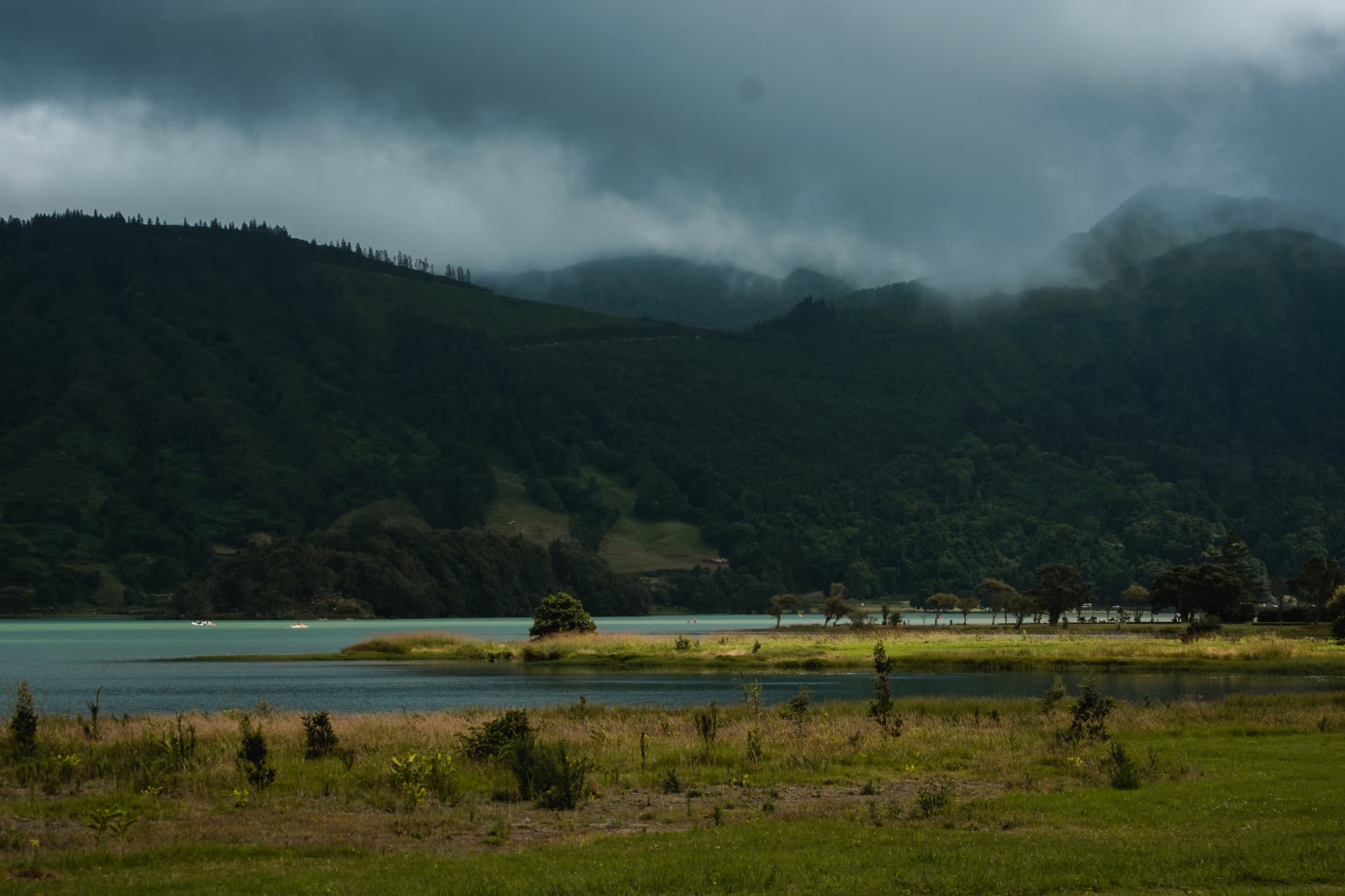 Turquoise lake beneath cloud-covered green hills