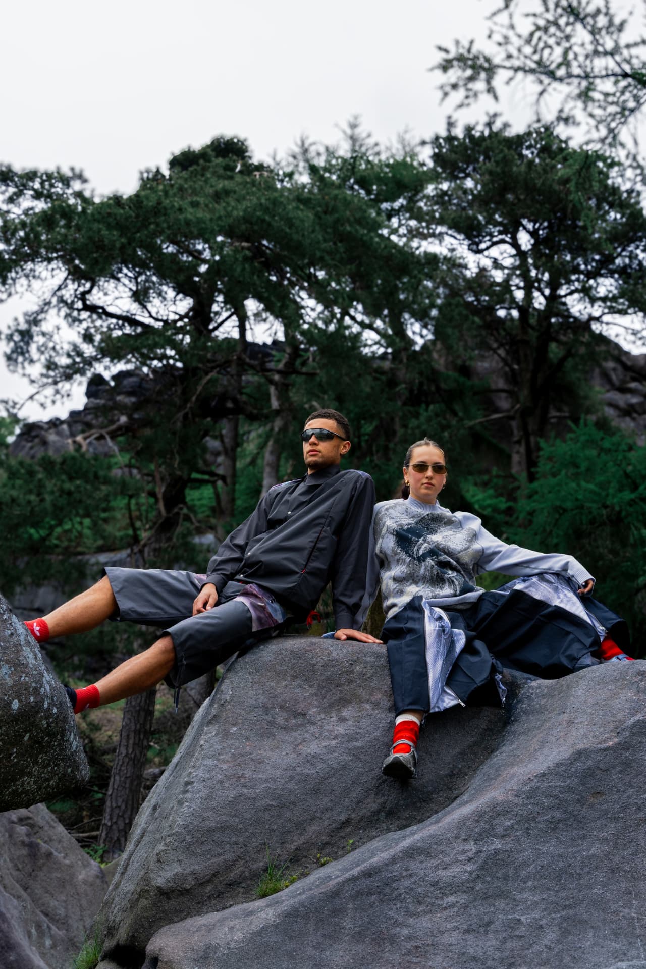 Two models reclining on boulders among pine trees