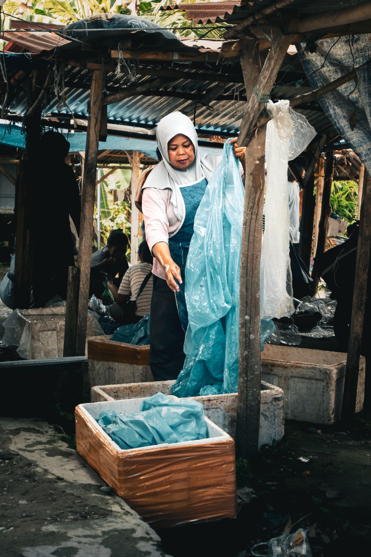 Market vendor in a headscarf holding a sheet of blue plastic at her stall