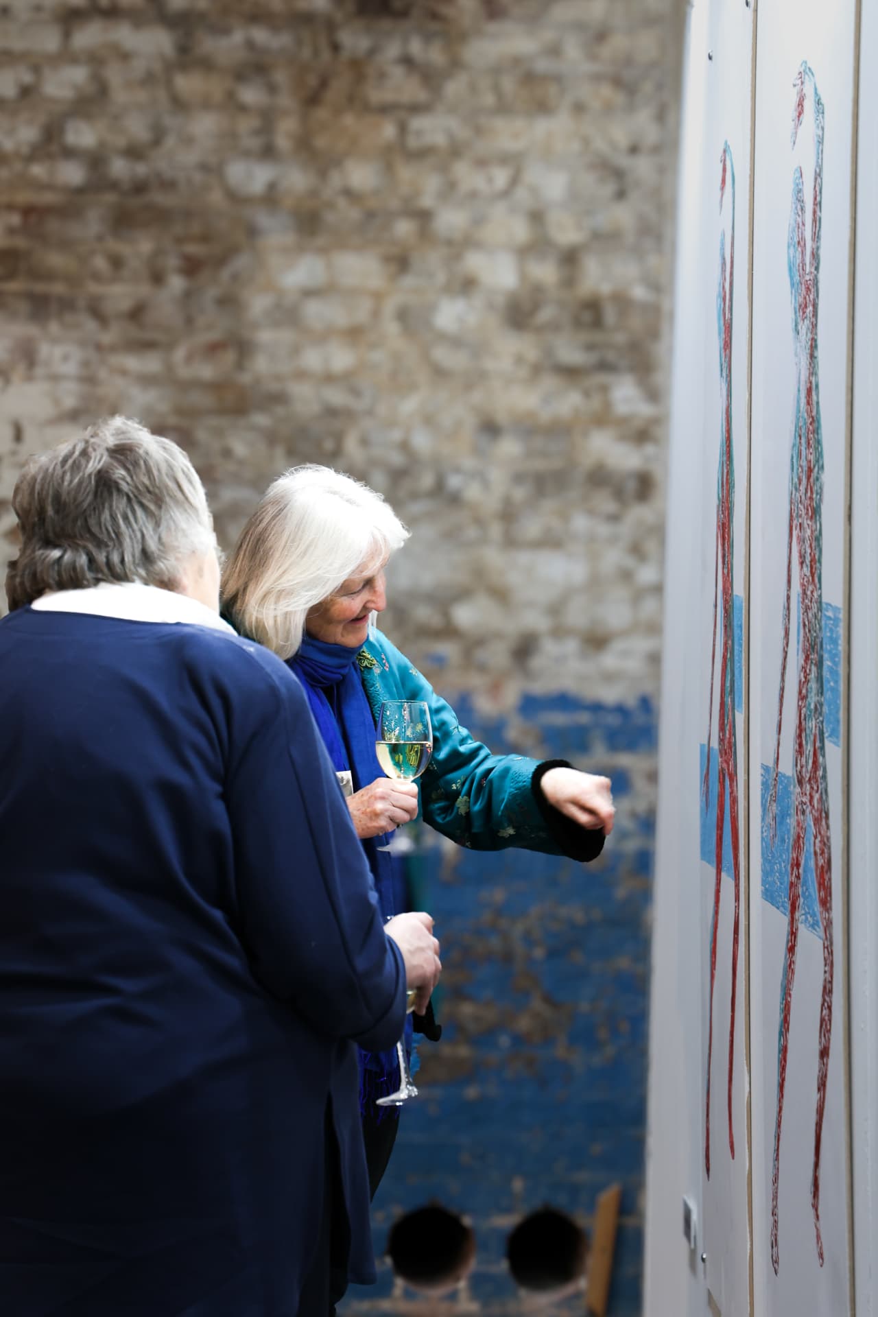 Two visitors examining prints against a brick wall