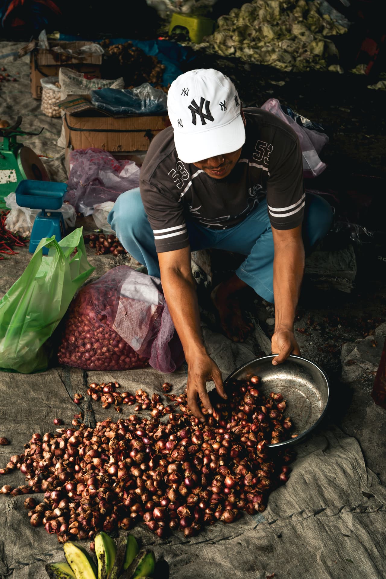 Vendor in a white cap sorting shallots at a market stall