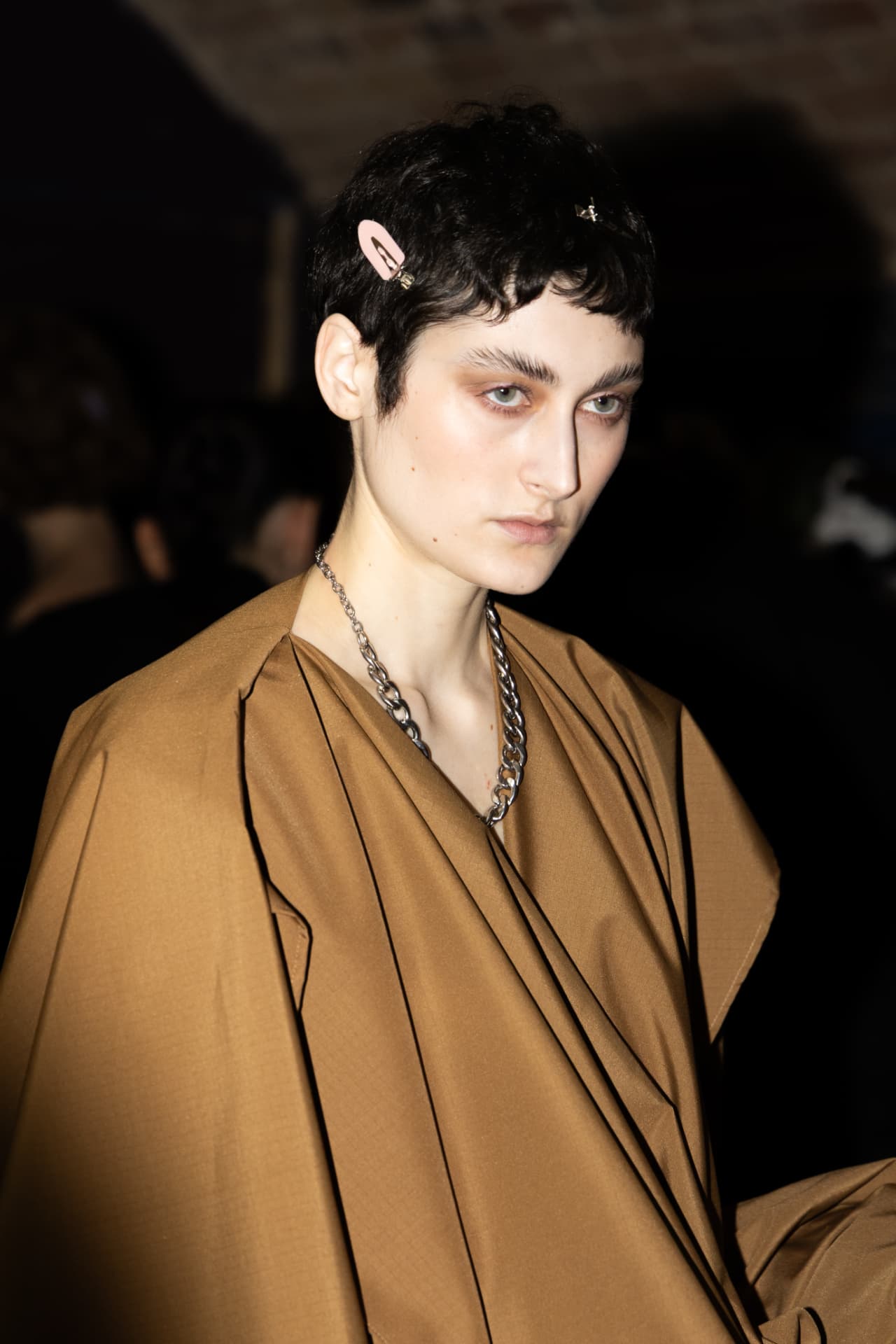 Model in tan draped coat with chain necklace