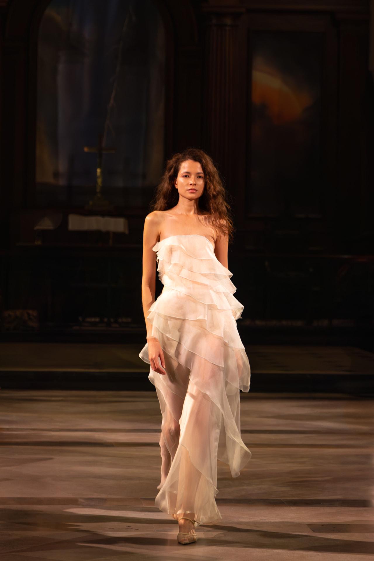 Model walking a runway in a tiered white dress