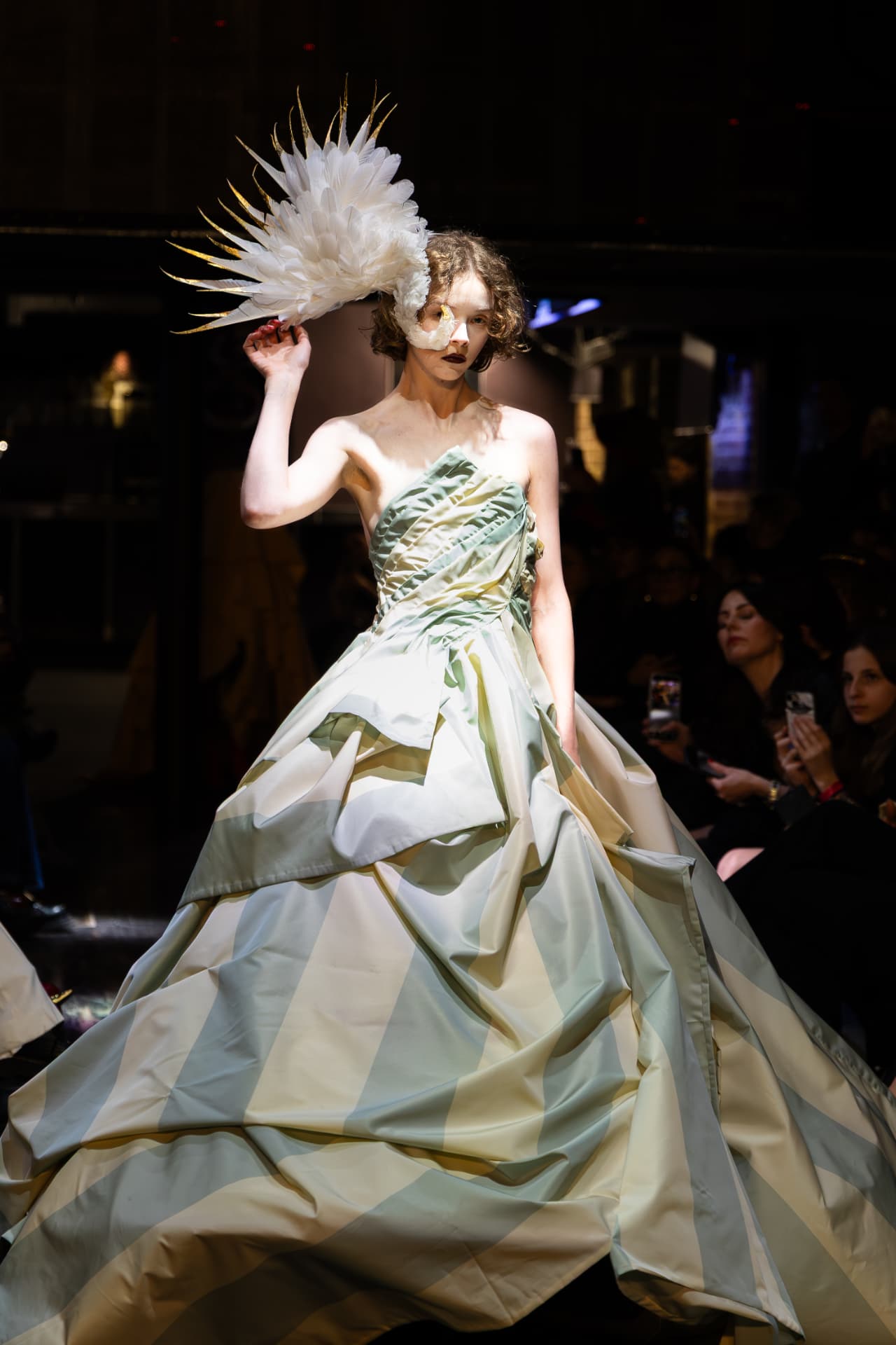 Model in a striped sage ball gown with a feathered headpiece