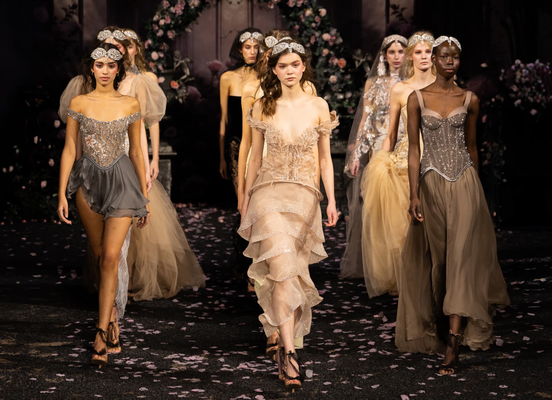 Models walking a petal-strewn runway in embellished couture gowns beneath floral arches