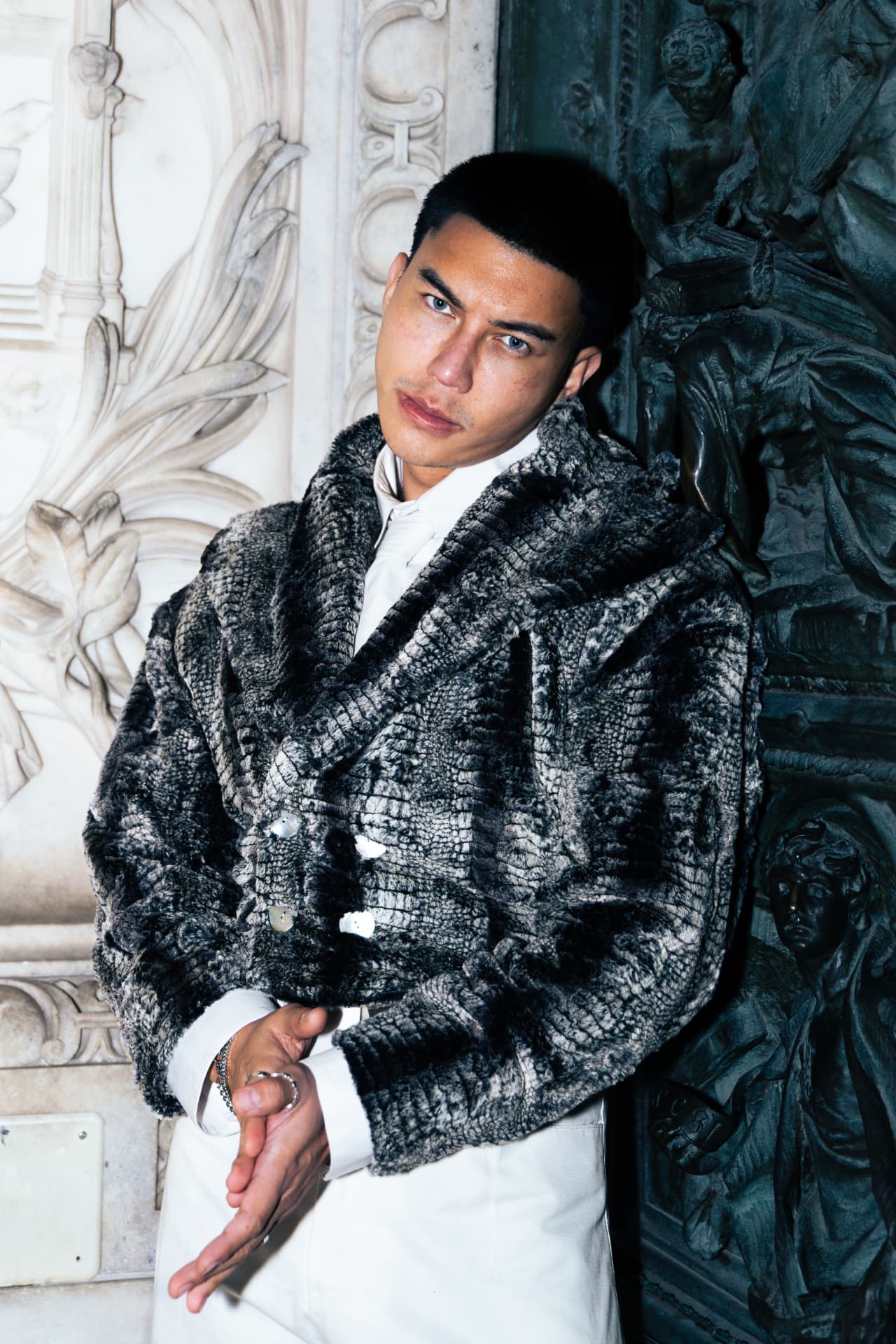 Model leaning against carved marble in a grey fur jacket