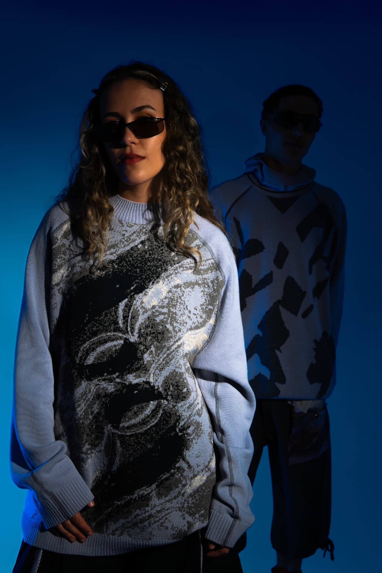 Two models in printed knitwear on a blue gradient backdrop