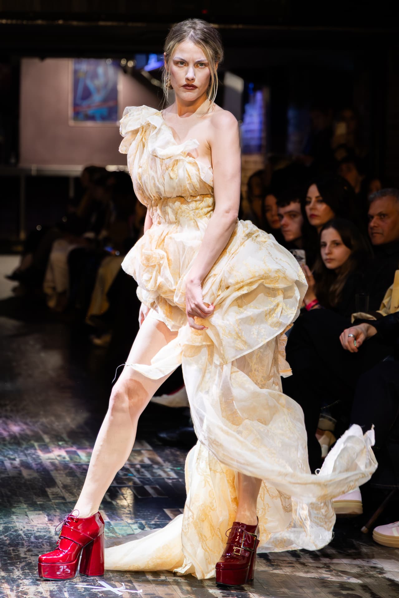 Model in a sculptural ruffled gown and red platform heels on the runway