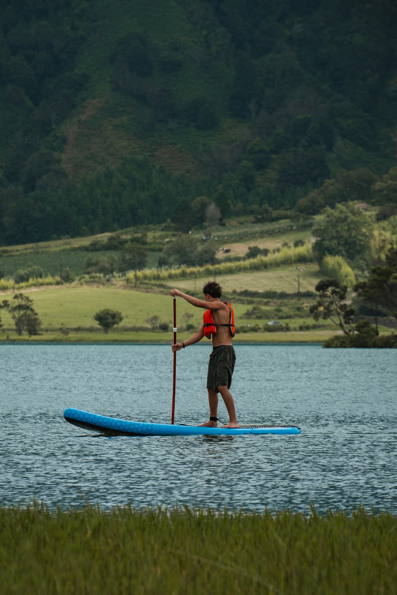 Man paddleboarding on a calm lake surrounded by green hills